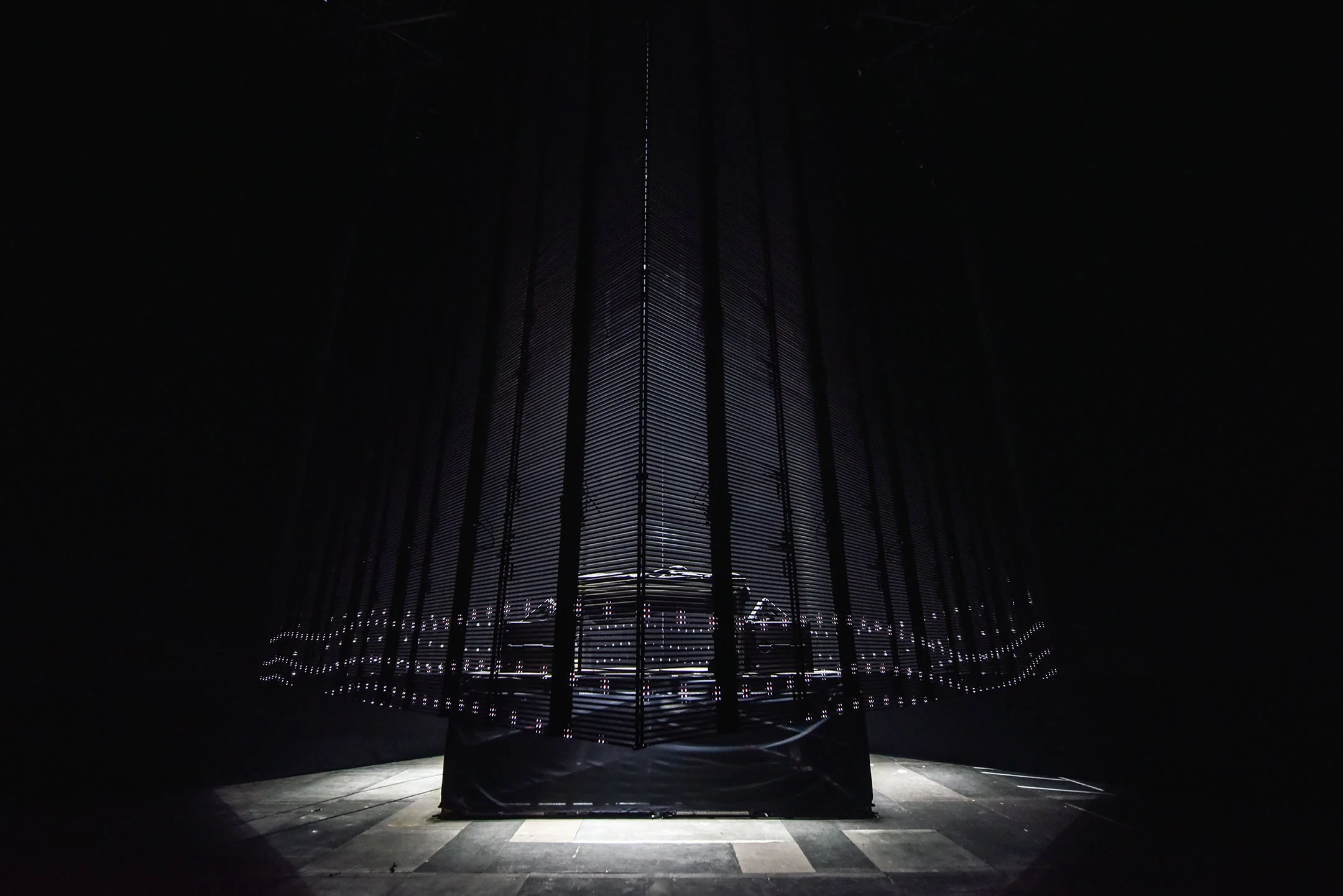 A dark installation with vertical black bars and illuminated horizontal lines, with light shining on the floor in front.