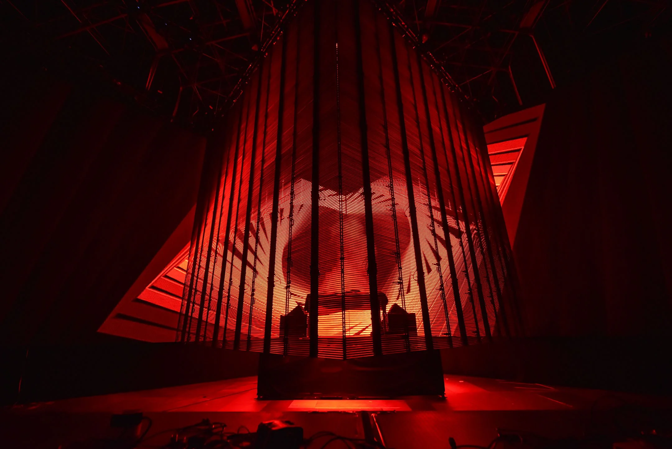 A large, vertical red-lit industrial machine with vertical bars and digital screens, inside a dark enclosed space.