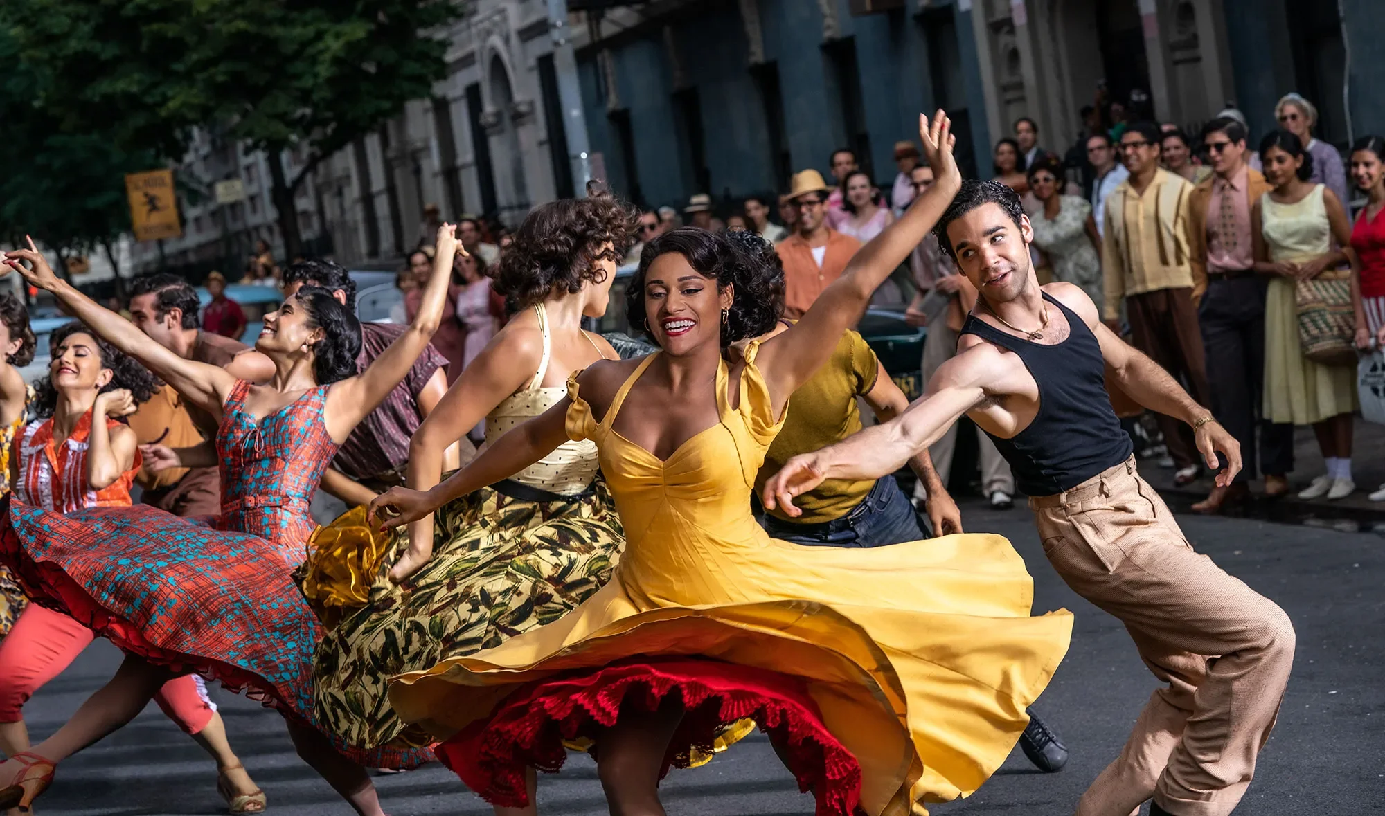 People dancing joyfully in colorful costumes during an outdoor cultural celebration in a city street.