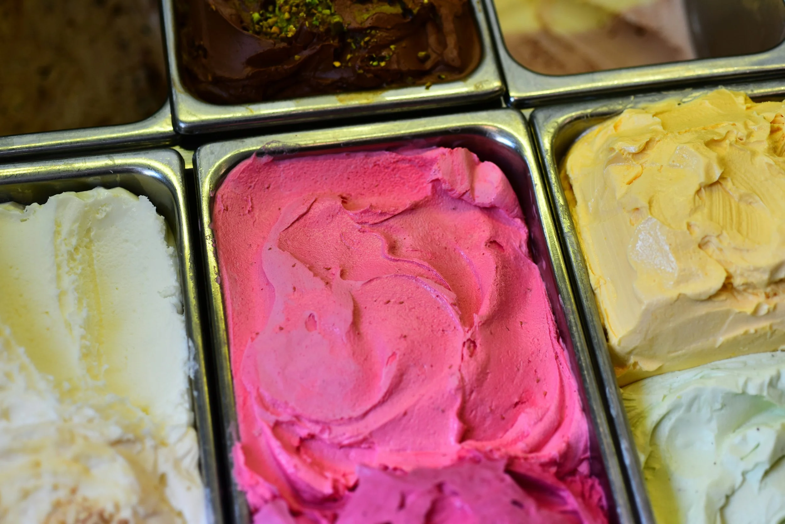 Four metal containers filled with different flavors of ice cream, including vanilla, strawberry, chocolate, and lemon.