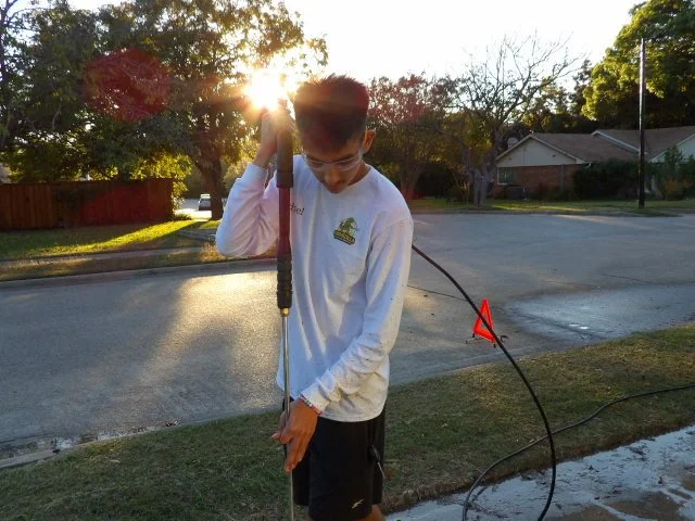 A young boy holding a long metal tool with one hand, standing outside on a residential street during sunset.