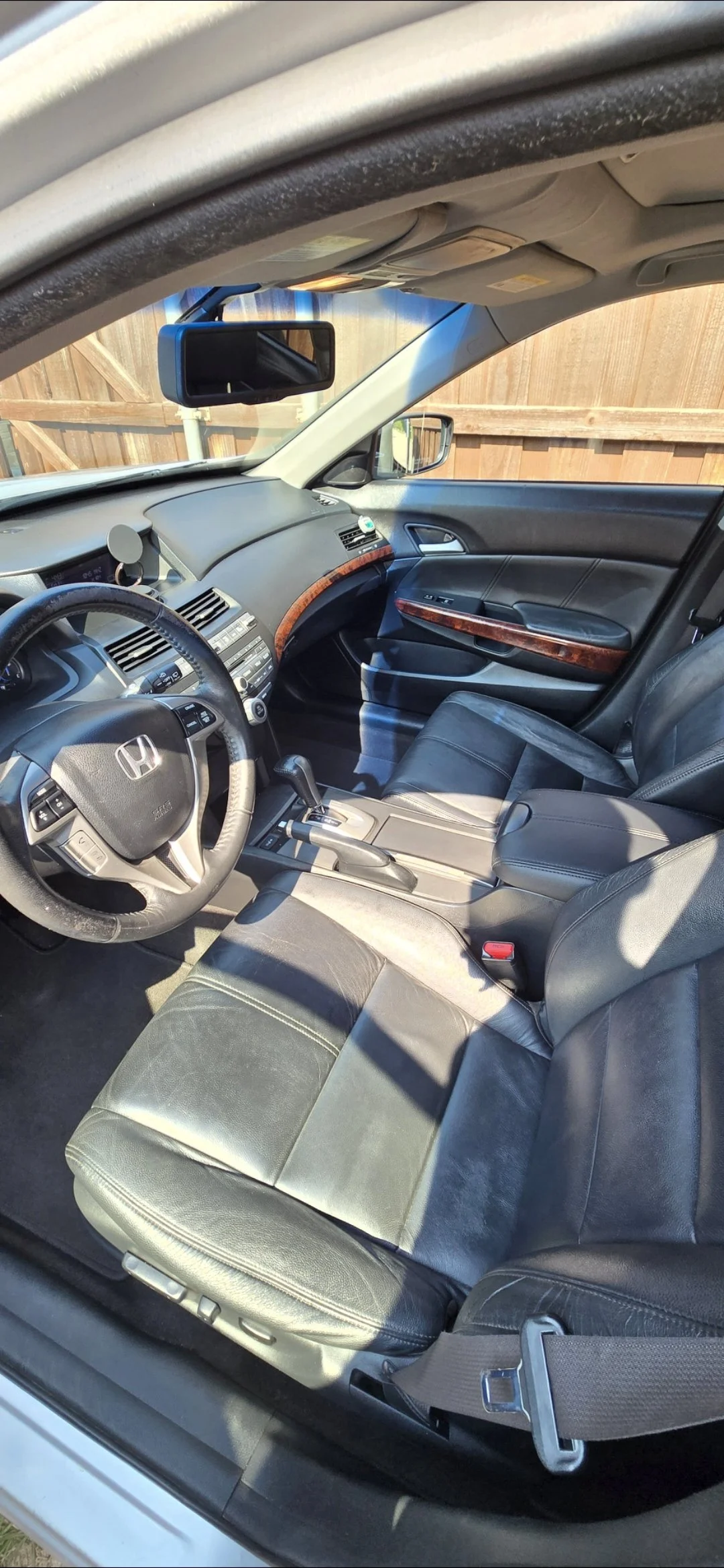 Interior of a car with black leather seats, a dashboard with wood grain accents, and a gear shift, taken from the open driver’s side door.