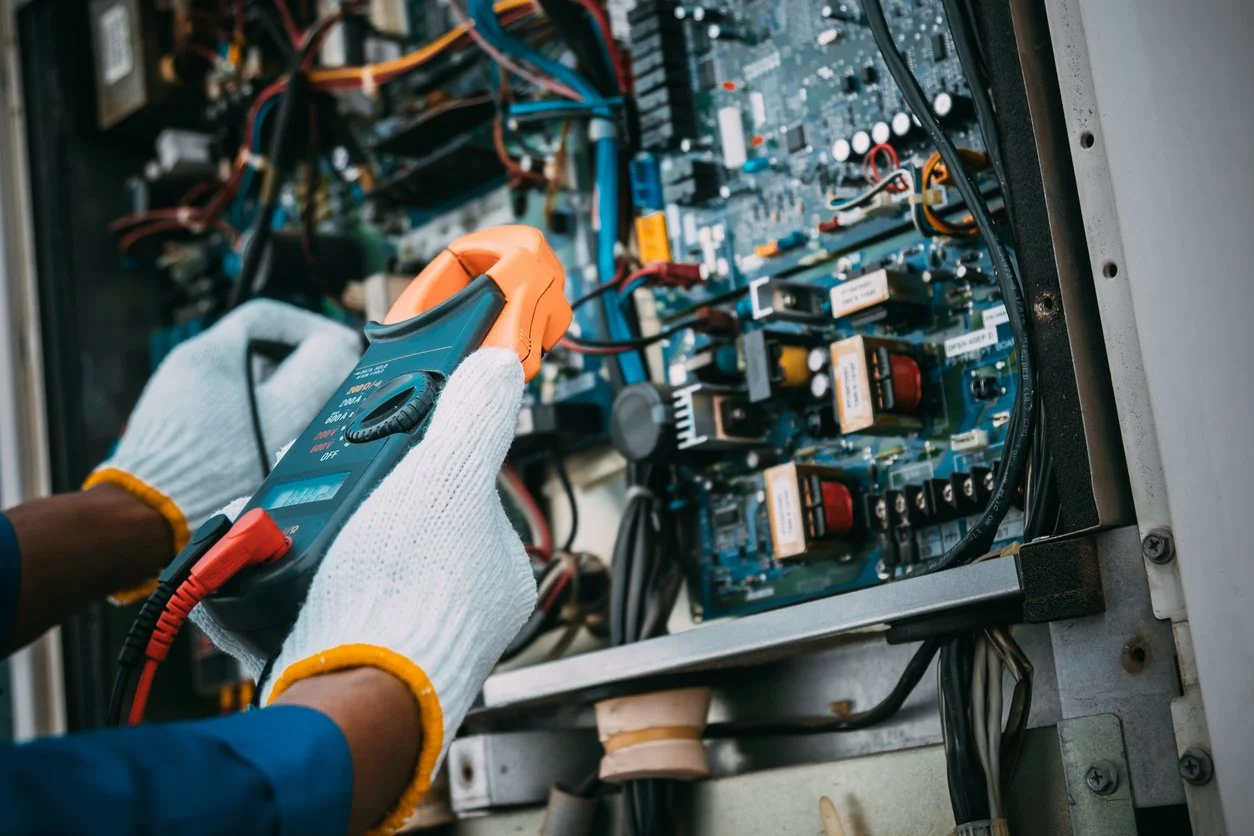 Person inspecting or repairing an electrical control panel with a digital multimeter.