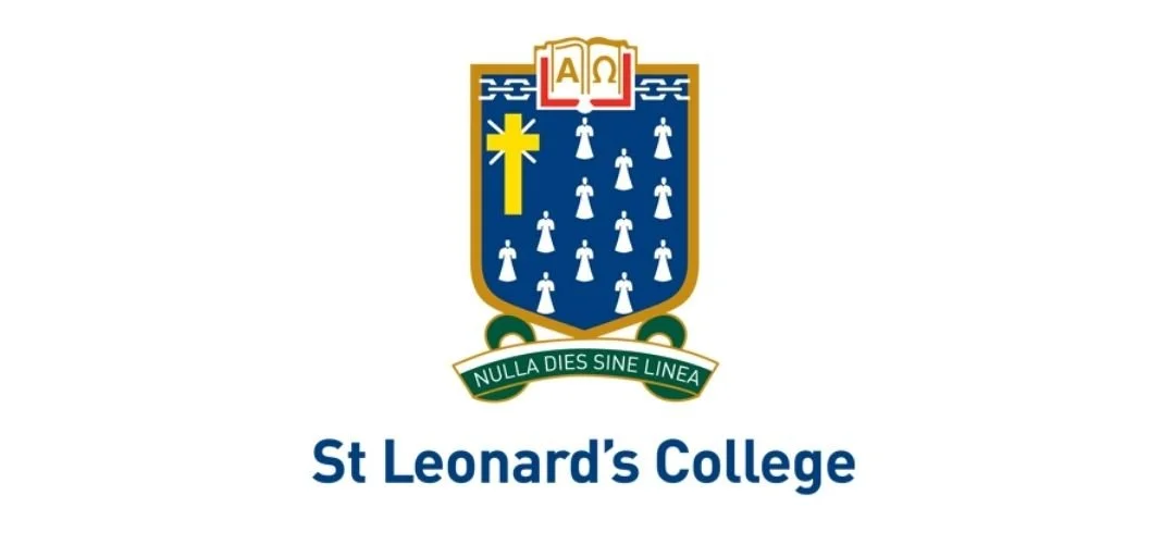 The coat of arms of St Leonard's College features a blue shield with a yellow cross and white angel figures, topped with an open book displaying Greek letters Alpha and Omega, and a motto ribbon below reading 'NULLA DIES SINE LINEA.' The image also includes the text 'St Leonard's College' beneath the coat of arms.