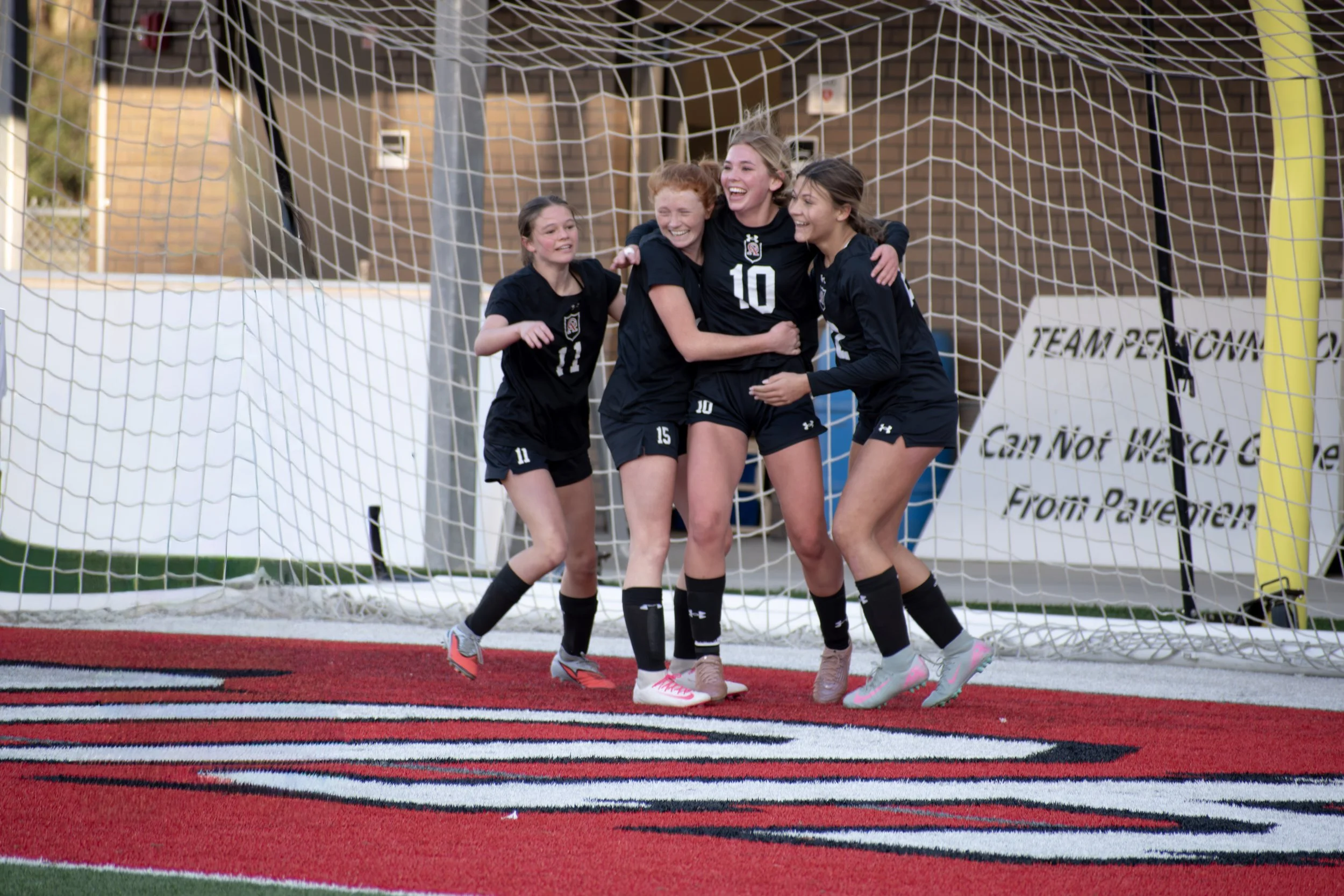 Four soccer players celebrating together on the field near the goalpost immediately after scoring a goal