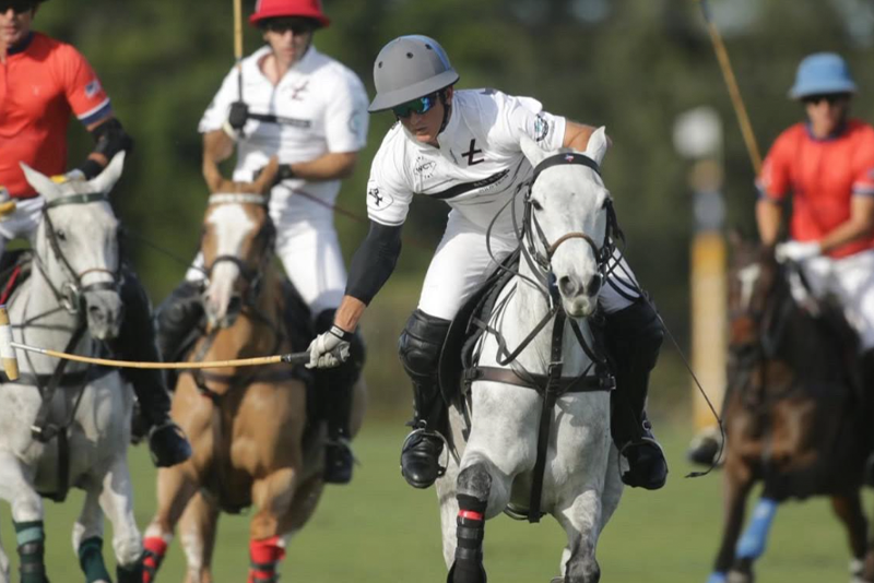 Group of polo players riding horses during a match, wearing helmets and jerseys.