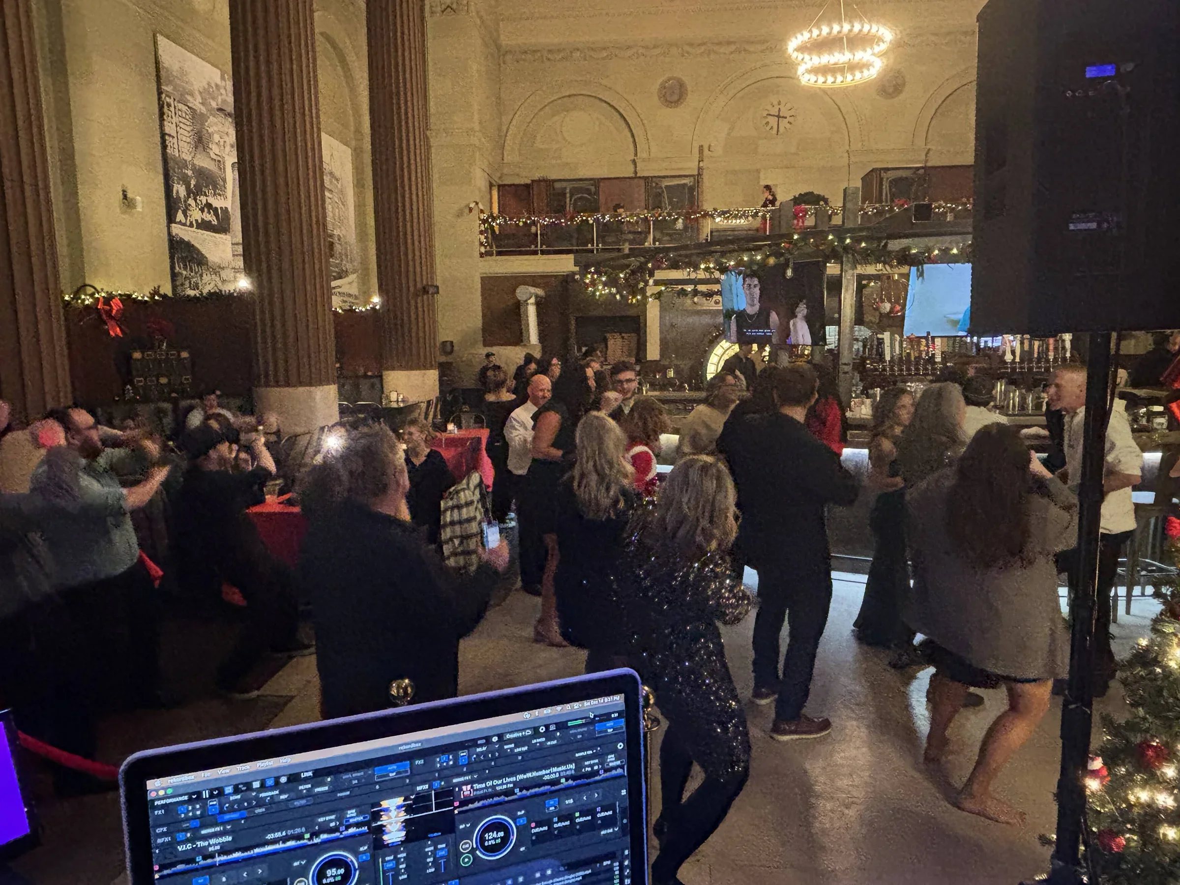 People dancing and socializing in a decorated indoor venue with Christmas lights, garlands, and a bar.