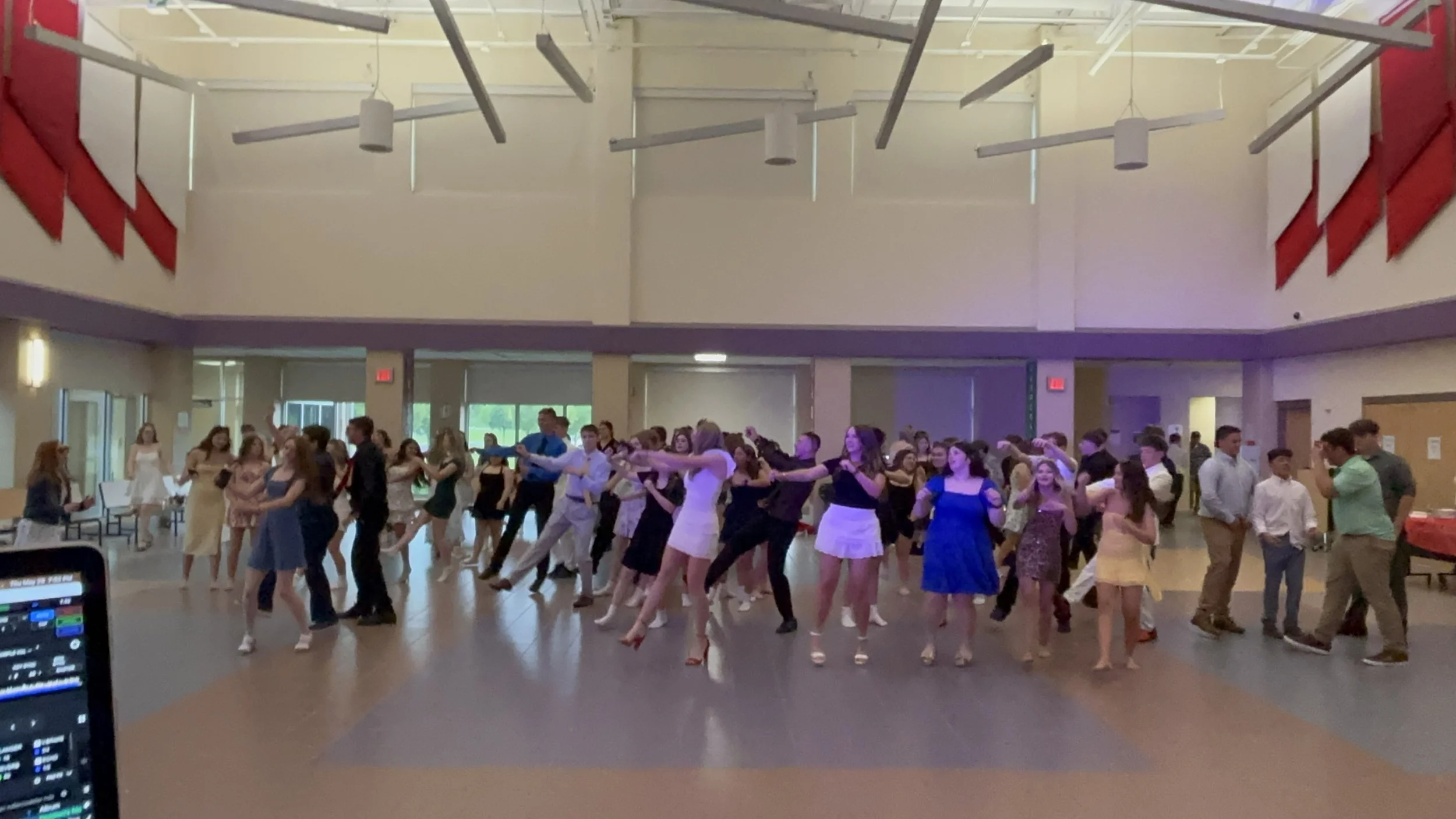 A group of young people dancing together in a large hall during a social event, with some couples dancing in the foreground and others in the background.