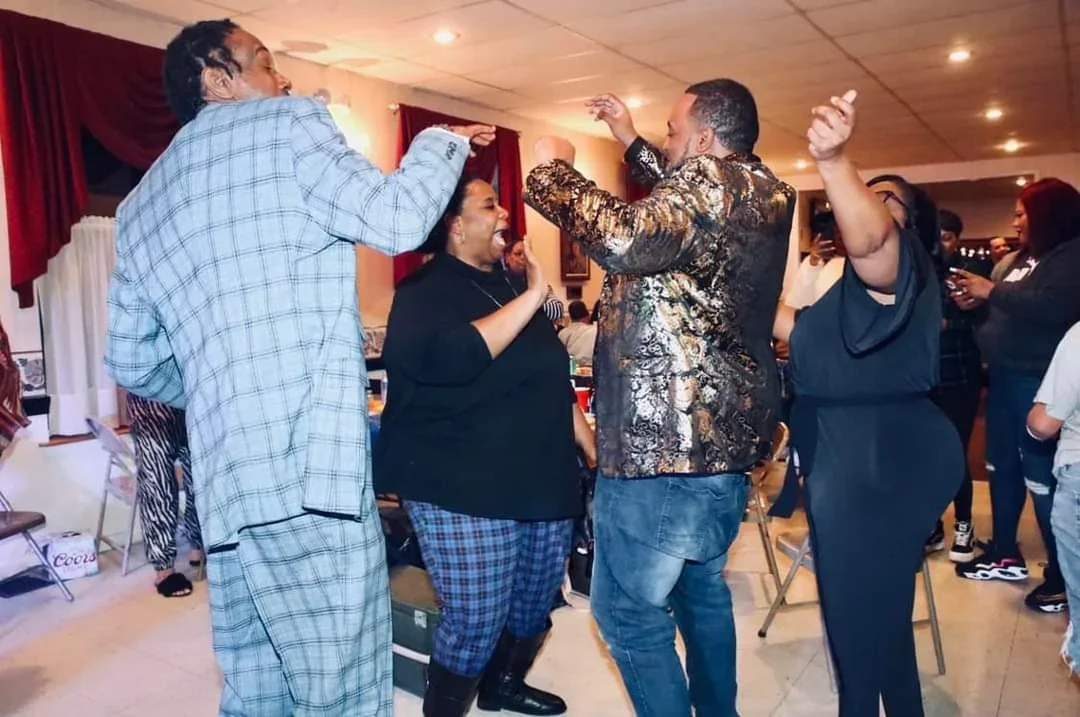 People dancing and having fun at a social gathering indoor, with some smiling and others taking photos.