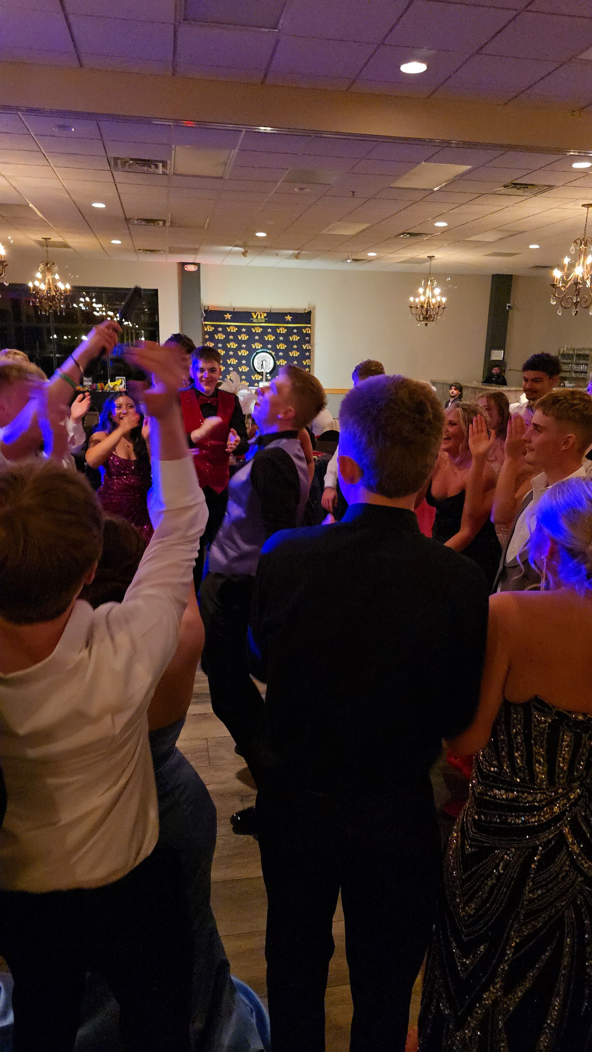 People dancing and socializing inside a bar or club with wooden walls, neon lights, and a mounted animal head and fur decorations on the wall.