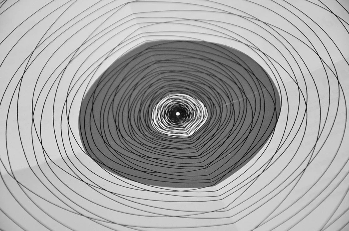 Abstract black and white concentric circles with a pink shading in the center, creating a spiral pattern.