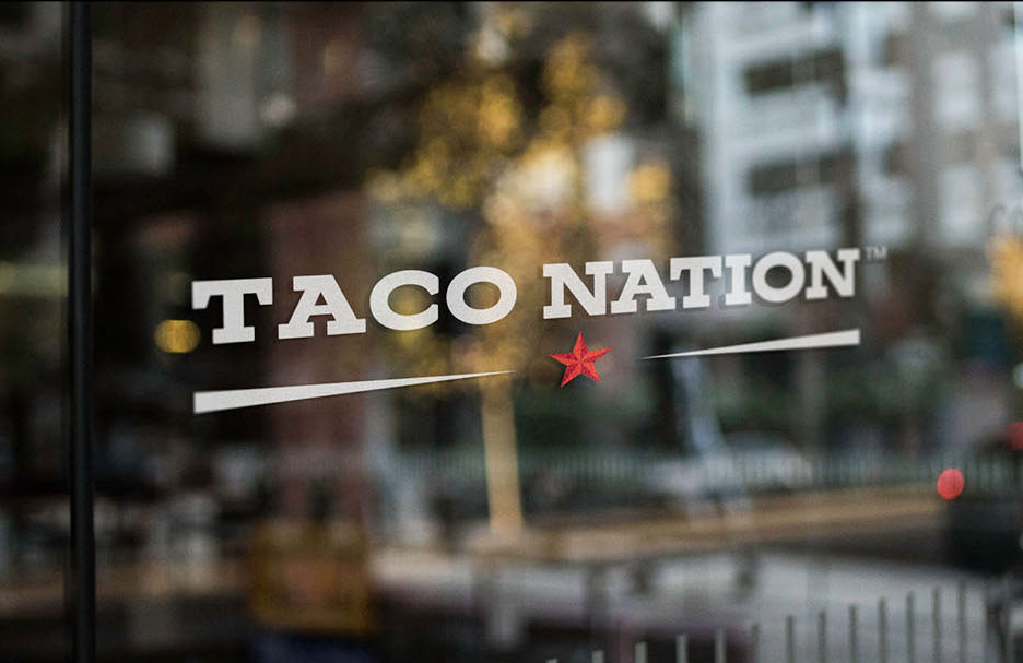 Close-up of a glass door with the Taco Nation logo, featuring white lettering, a red star, and a horizontal line.