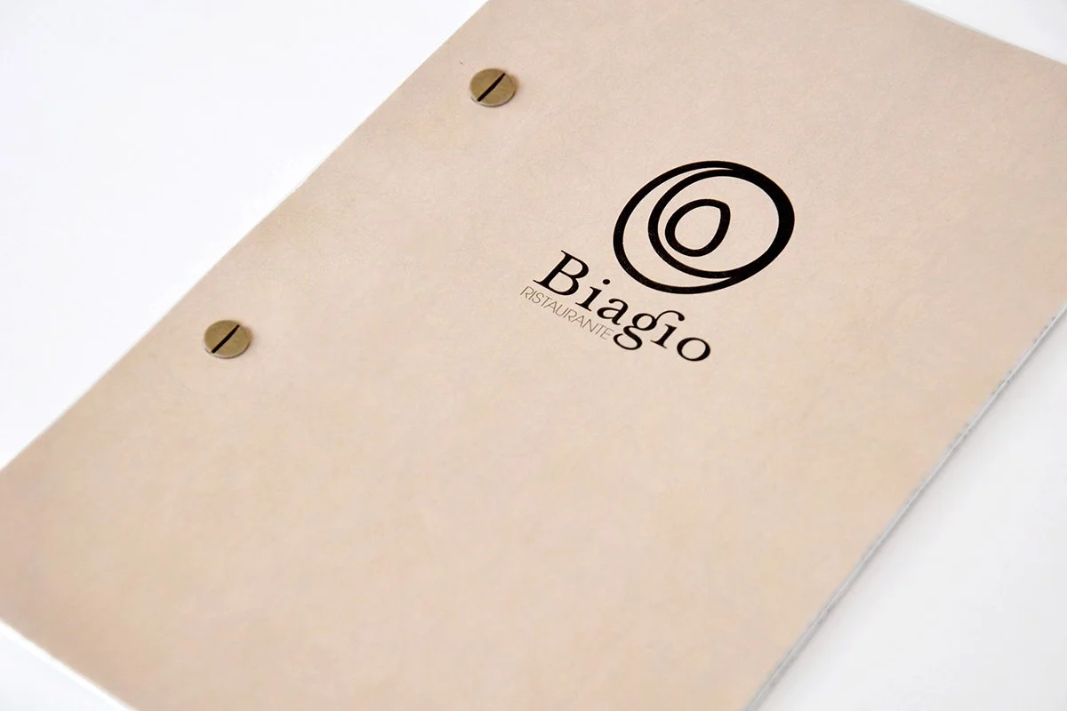 Close-up of a beige menu cover with the logo and name 'Biagio Ristorante' printed on it, secured with two brass-colored screws.