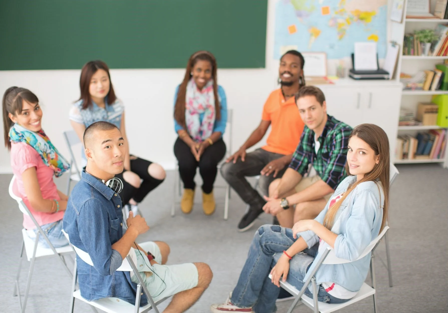 A group of students sitting in a classroom, in a round circle with a chalkboard behind them