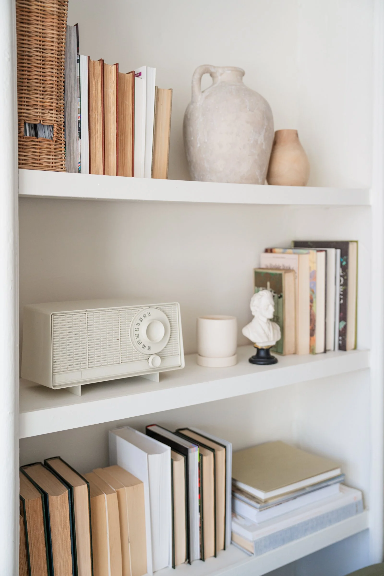 White bookshelf with books, vintage radio, small bust sculpture, and decorative vases.