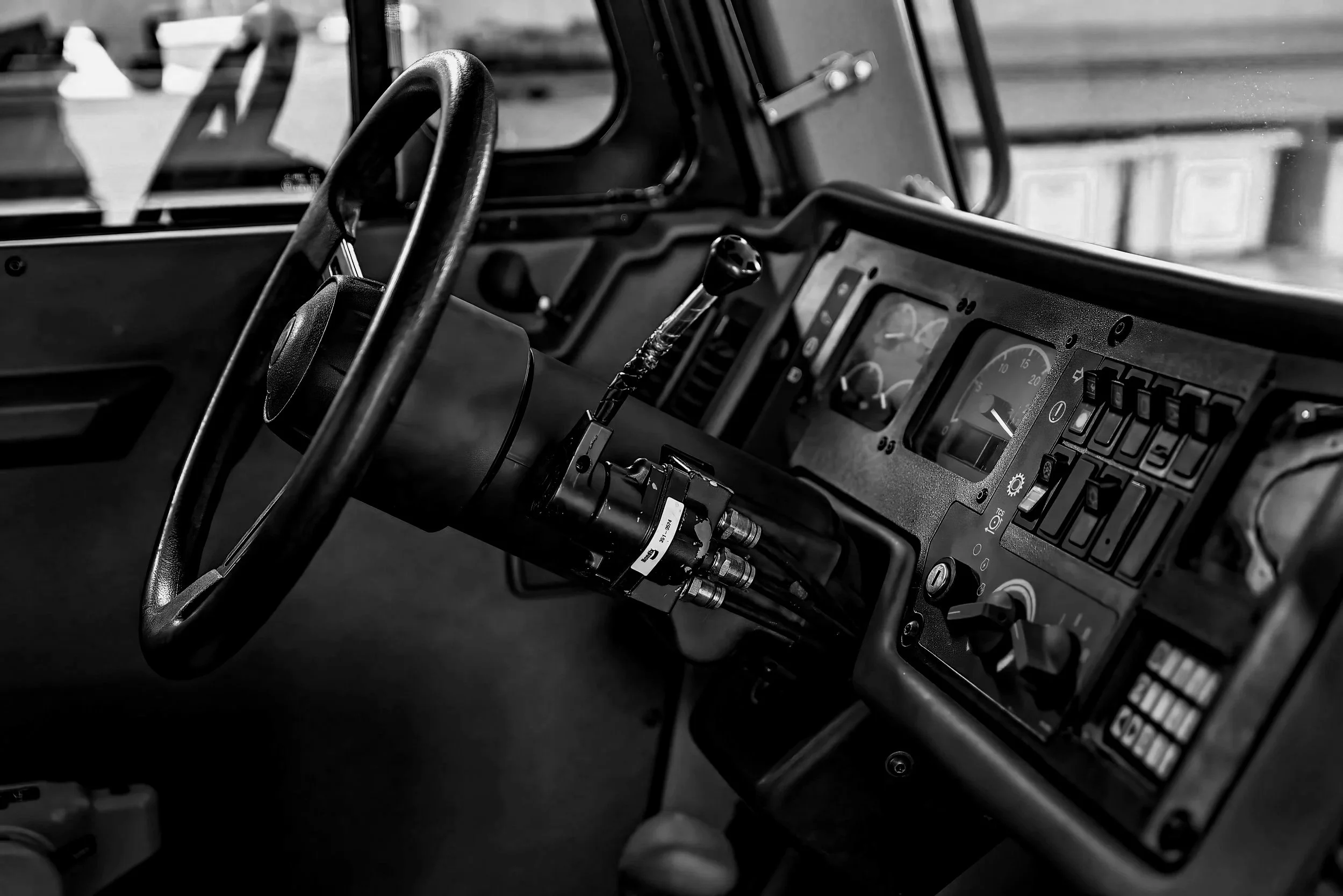Black and white photo of a vehicle's dashboard and steering wheel, with various gauges, switches, and controls.