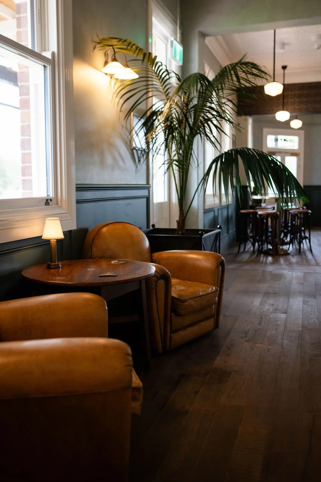 A kitchen counter with a bouquet of pink and purple flowers in a white vase, a French press coffee maker, a small white cup, two wooden salt and pepper shakers, a loaf of bread, a cutting board, and miscellaneous small items. There are wooden wall panels, electrical outlets, and switches on the wall behind.