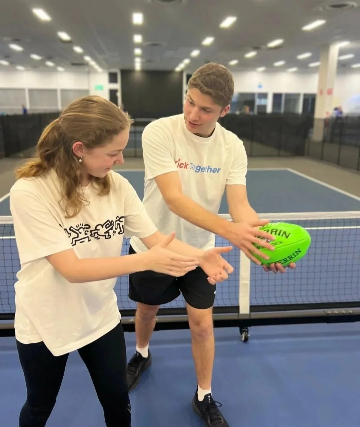 Two KickTogether coaches on an indoor court with a bright green ball.