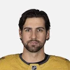 Headshot of a man with dark hair and beard wearing a yellow sports jersey.