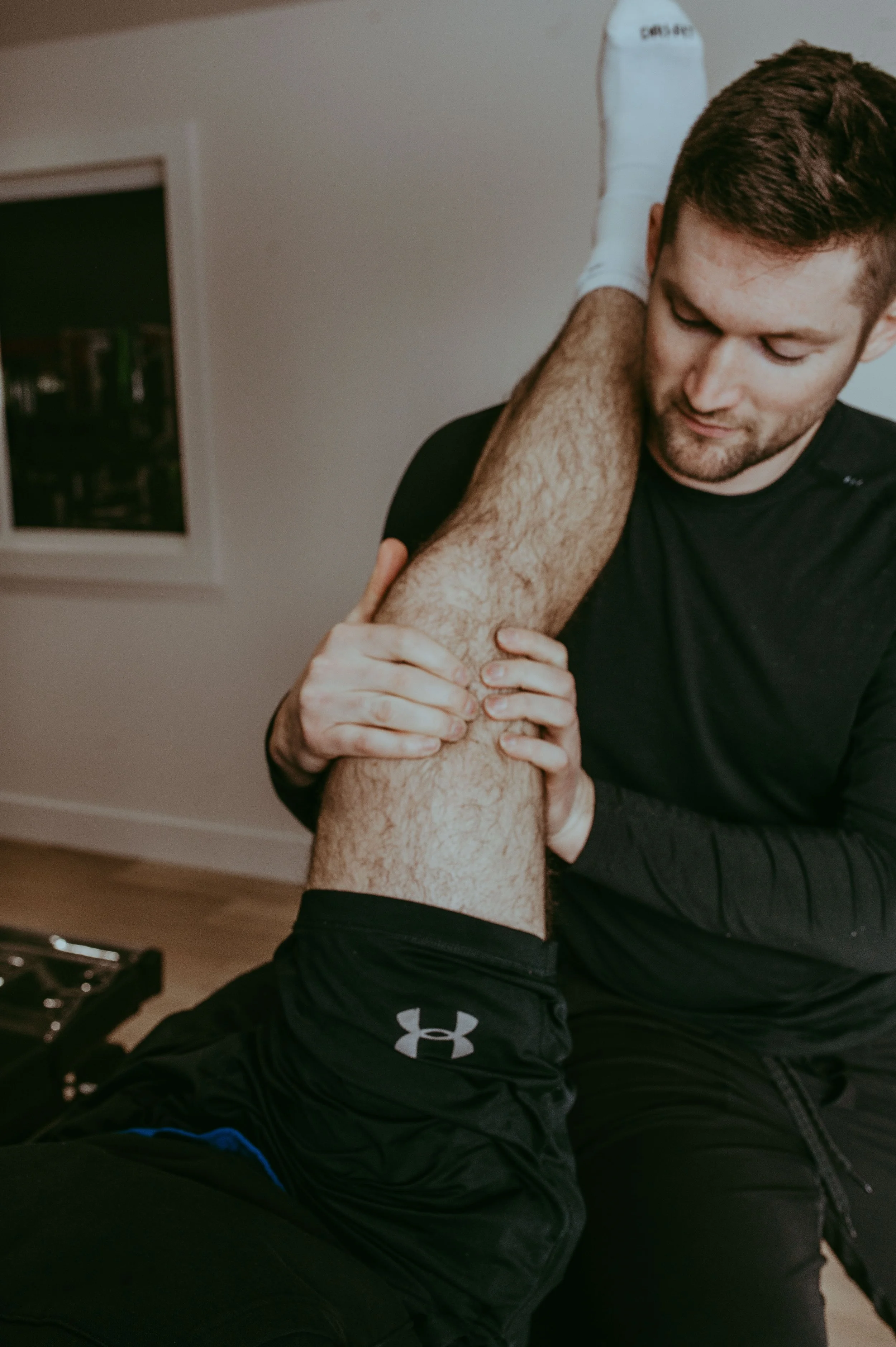 A man receiving physical therapy or stretching therapy on his leg from a physiotherapist in an indoor setting.