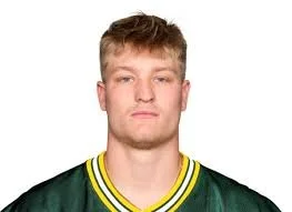 Portrait of a young man with short light brown hair, wearing a green sports jersey with yellow and white accents