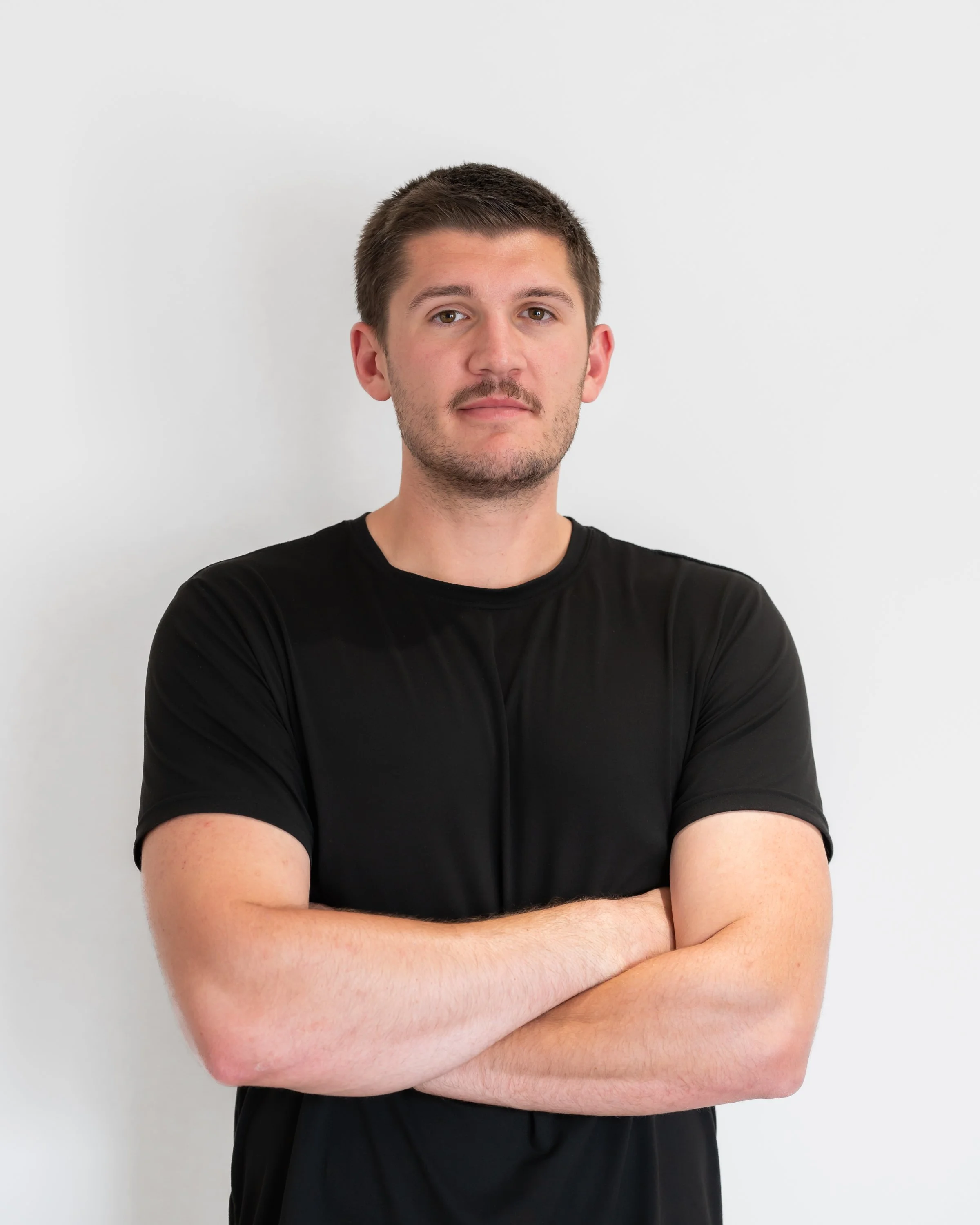 A woman with shoulder-length black hair smiling outdoors with green foliage in the background.