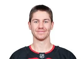 Headshot of a young man with short brown hair and a slight smile, wearing a black sports jersey with red accents.