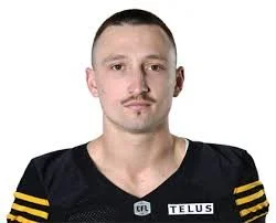 Portrait of a man with short hair and a mustache wearing a black sports jersey with yellow stripes on the shoulders, against a white background.