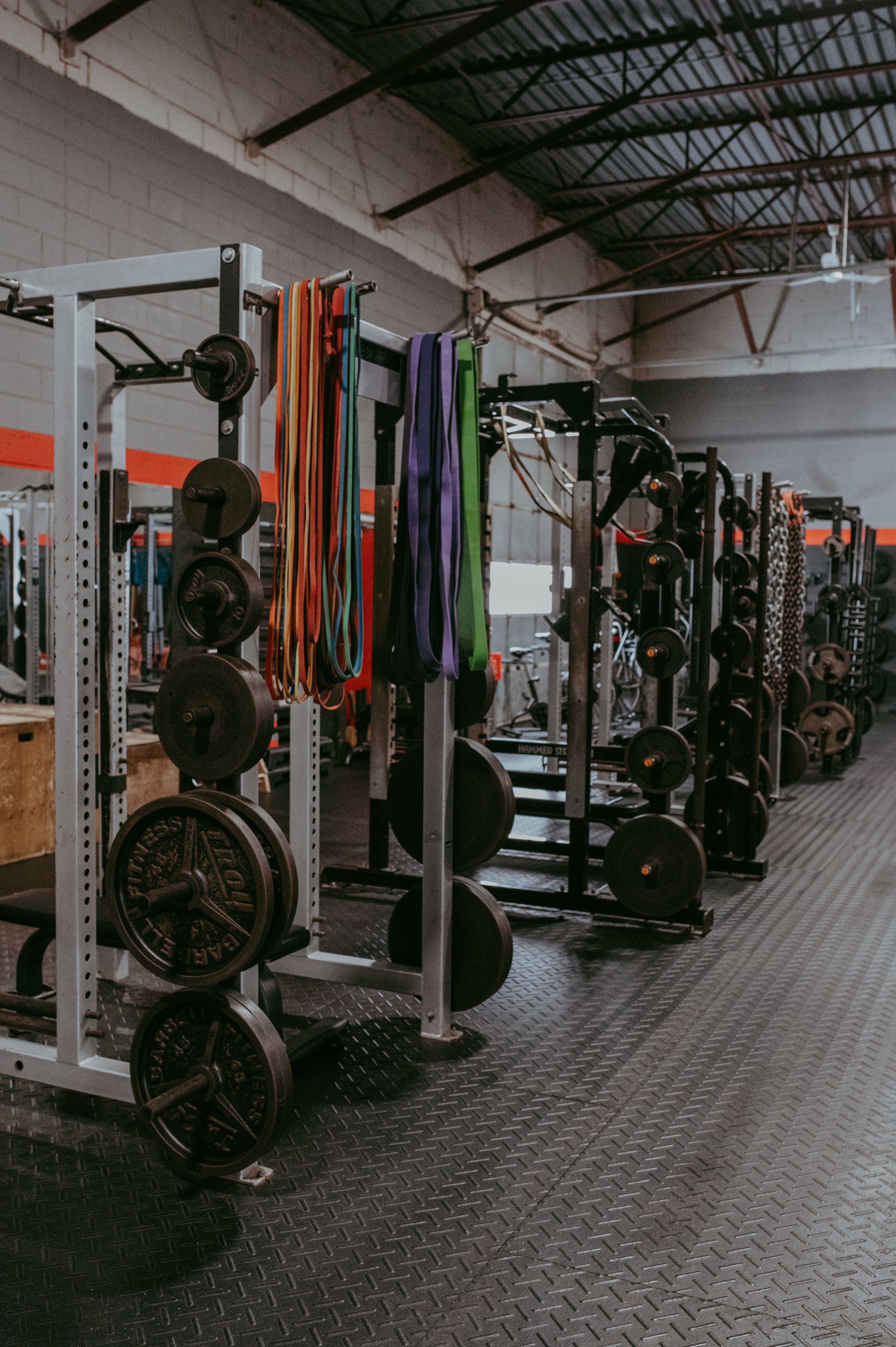 Gym equipment including weight plates, barbells, resistance bands, and weight racks in a fitness gym setting.