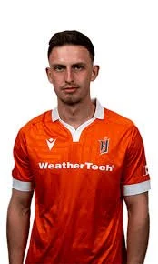 A young man wearing an orange sports jersey with white accents and a logo reading 'WeatherTech'.