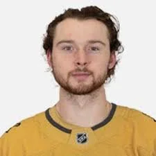 Portrait of a young man with curly hair and a beard, wearing a yellow hockey jersey.
