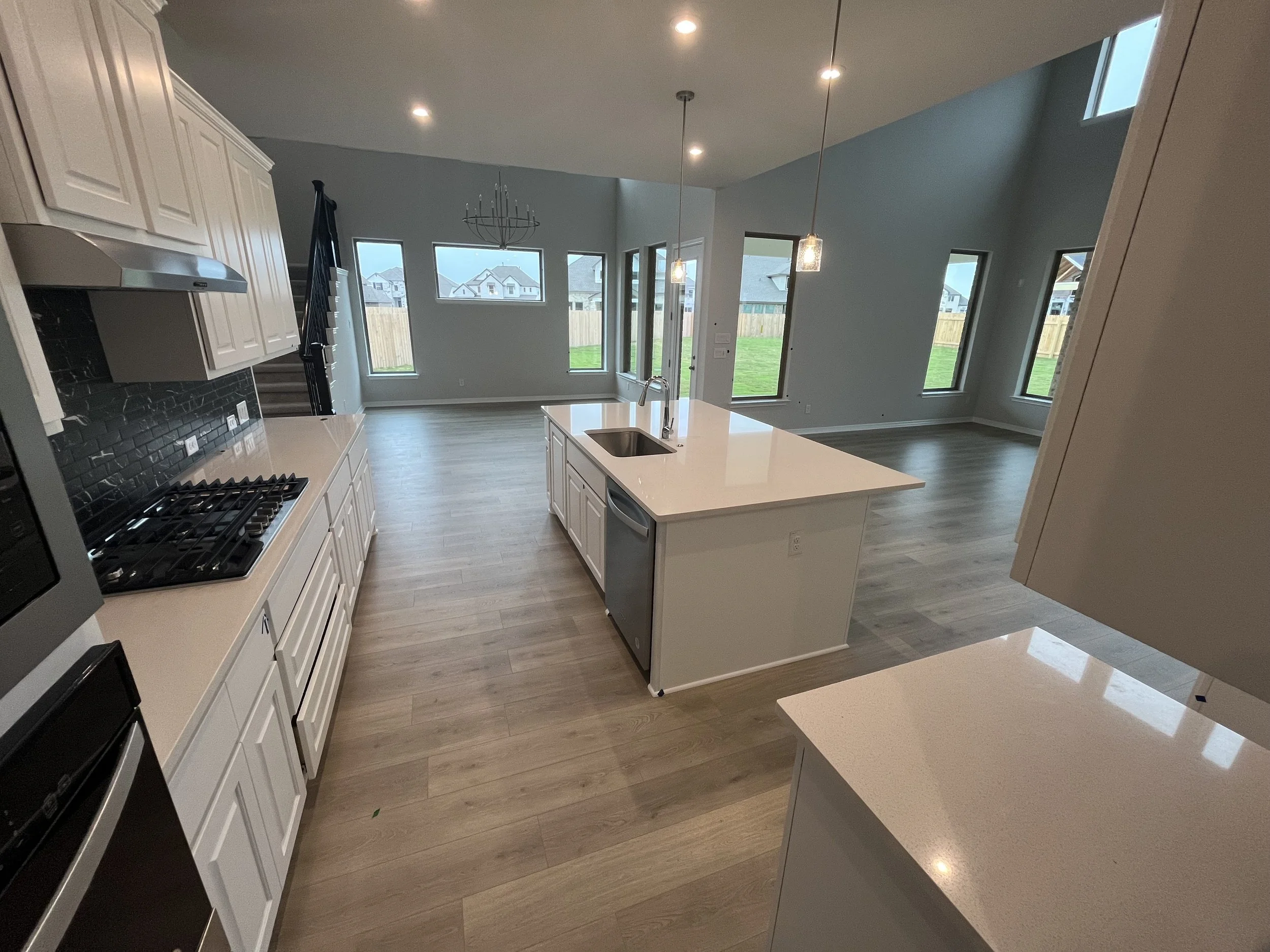 Open-concept kitchen and living area with white cabinets, a kitchen island, large windows, and hardwood floors.