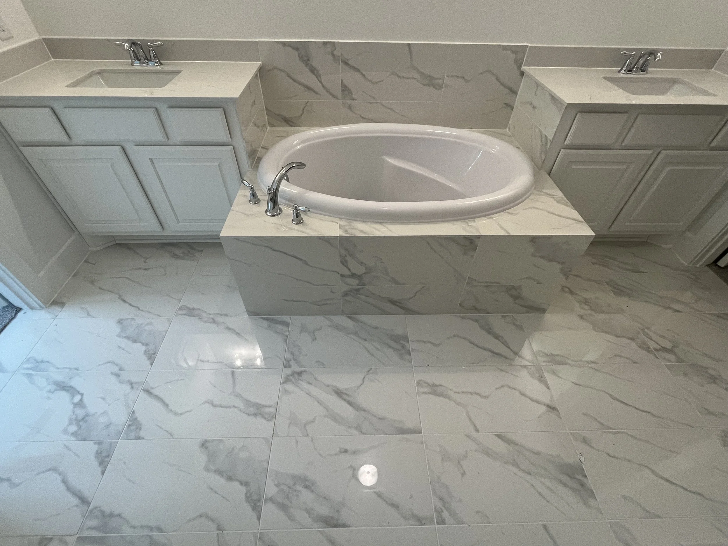 Bathroom with a built-in bathtub surrounded by marble tiles, with two sinks on either side with white cabinets and marble countertops.