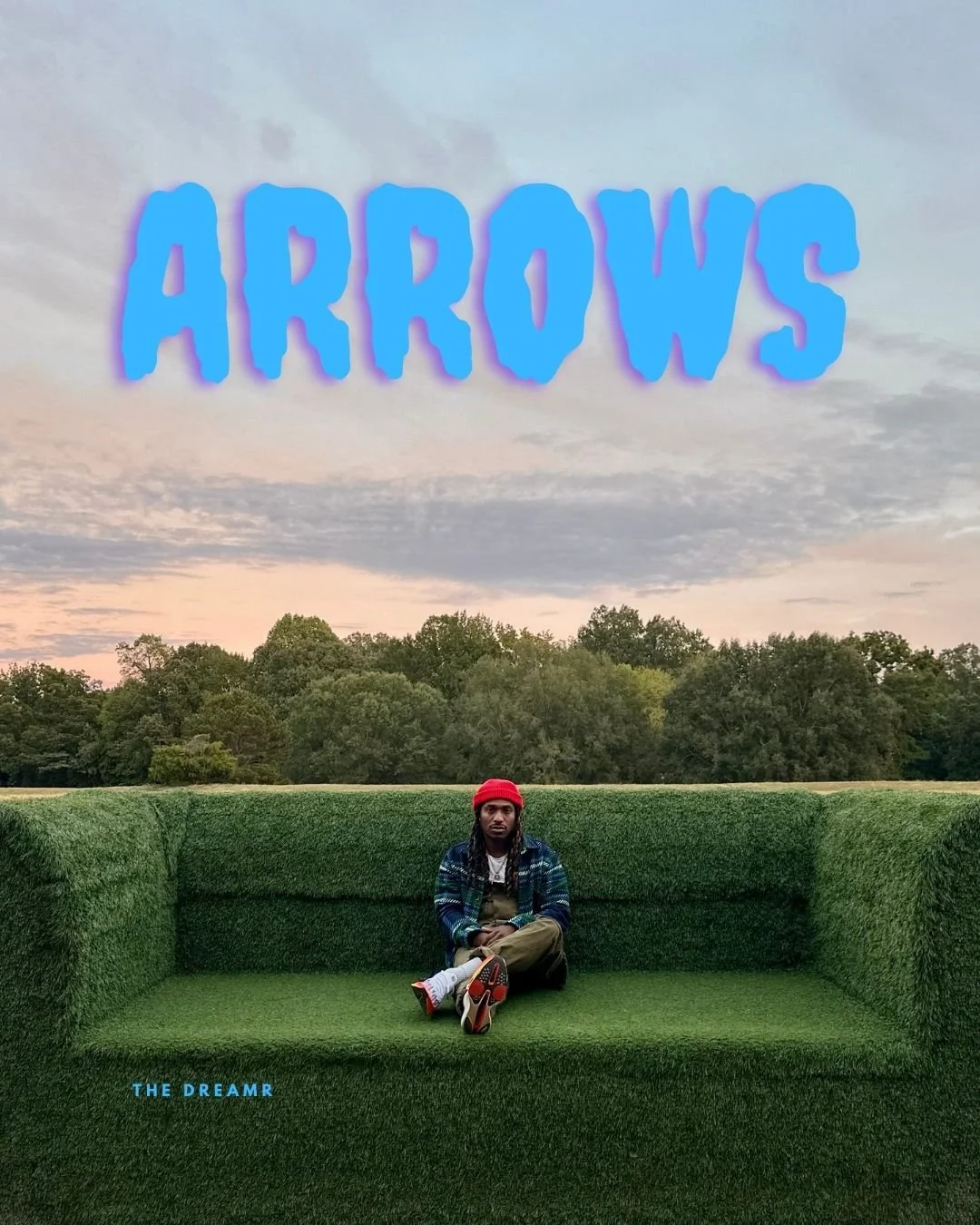 The DreamR sitting on a TV-shaped bench covered with green artificial grass in an outdoor park during sunset. The word 'ARROWS' appears in large blue text at the top, and 'THE DREAMR' is written in smaller blue text at the bottom left.