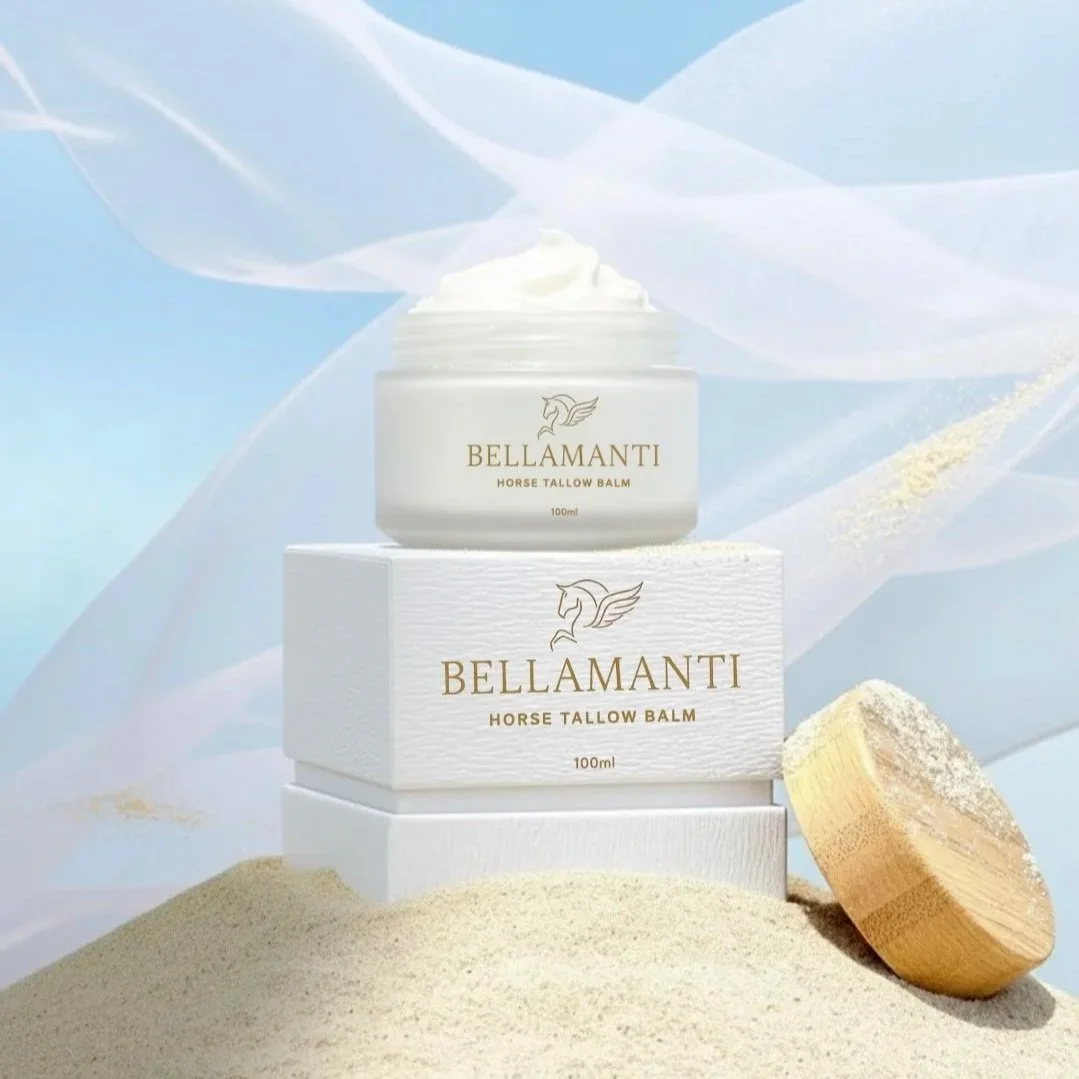 A jar of Bellamanti Horse Tallow Balm on top of a white box, with a wooden spoon and horse tallow around it, set against a soft, abstract background.