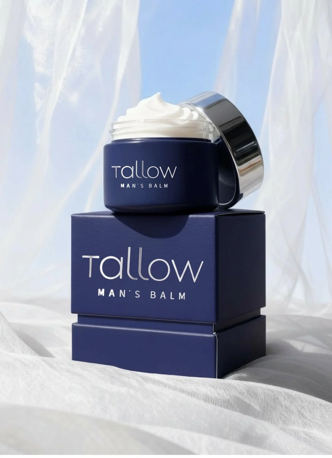 A jar of Tallow Man's Balm with a silver lid, placed on top of its matching blue box, against a light, textured background with light blue and white abstract patterns.