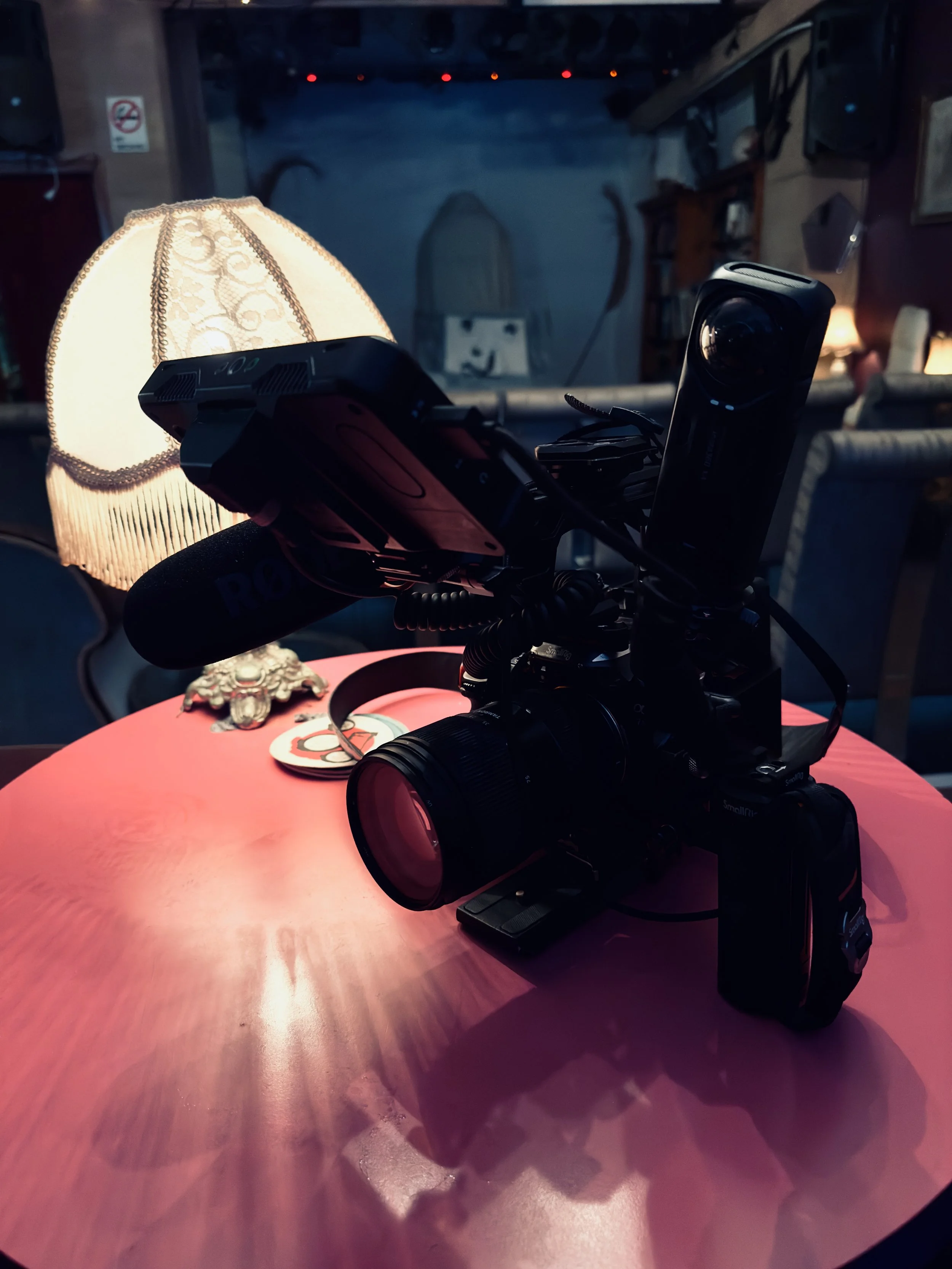 Camera setup on a pink table in a dimly lit room with a lampshade and scattered decorative items in the background.