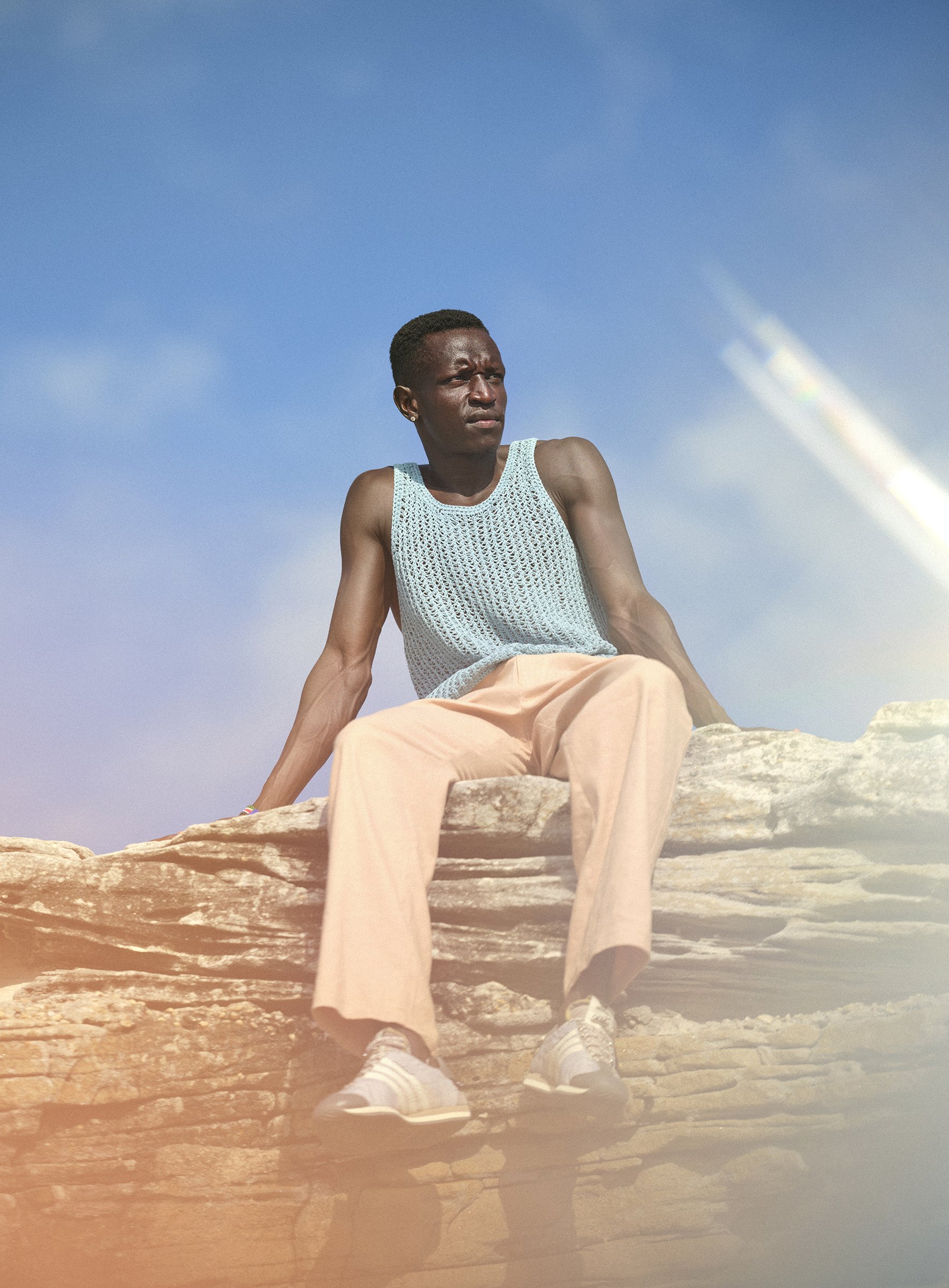 Peter Bol photographed for Esquire Magazine, styled in sunglasses and captured seated on the clifftops of Clovelly Beach.