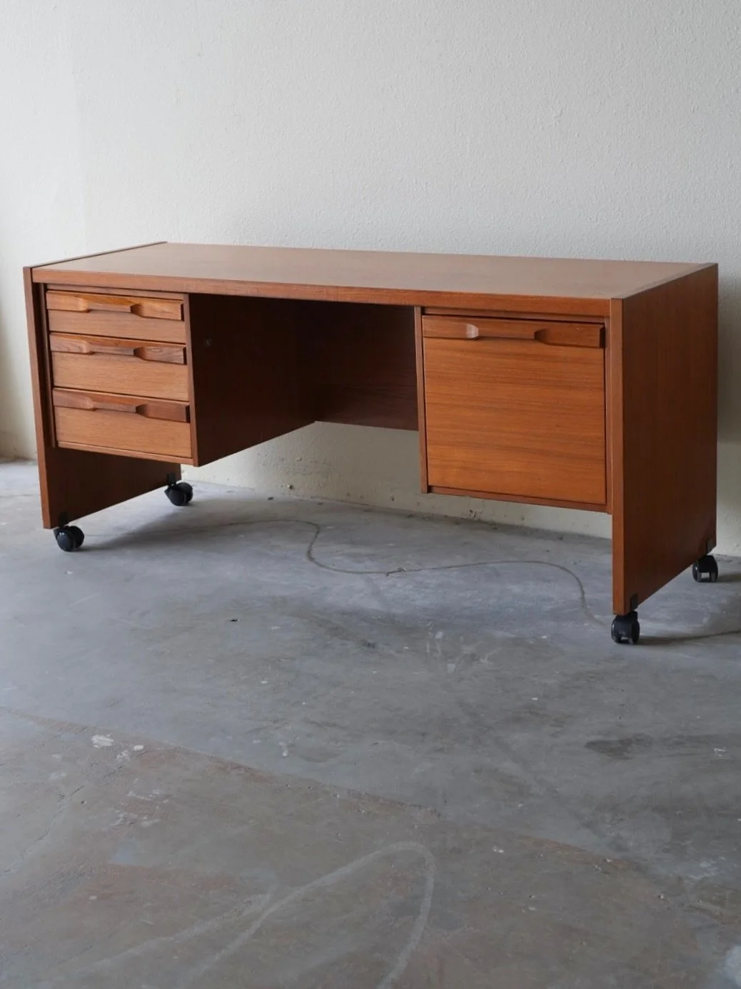 Danish teak desk crafted by Denka Mobler

This beautifully preserved piece features a rich teak finish with a sleek, minimalist aesthetic characteristic of the era. 

It includes three drawers on the left side and a single deep drawer on the right. T