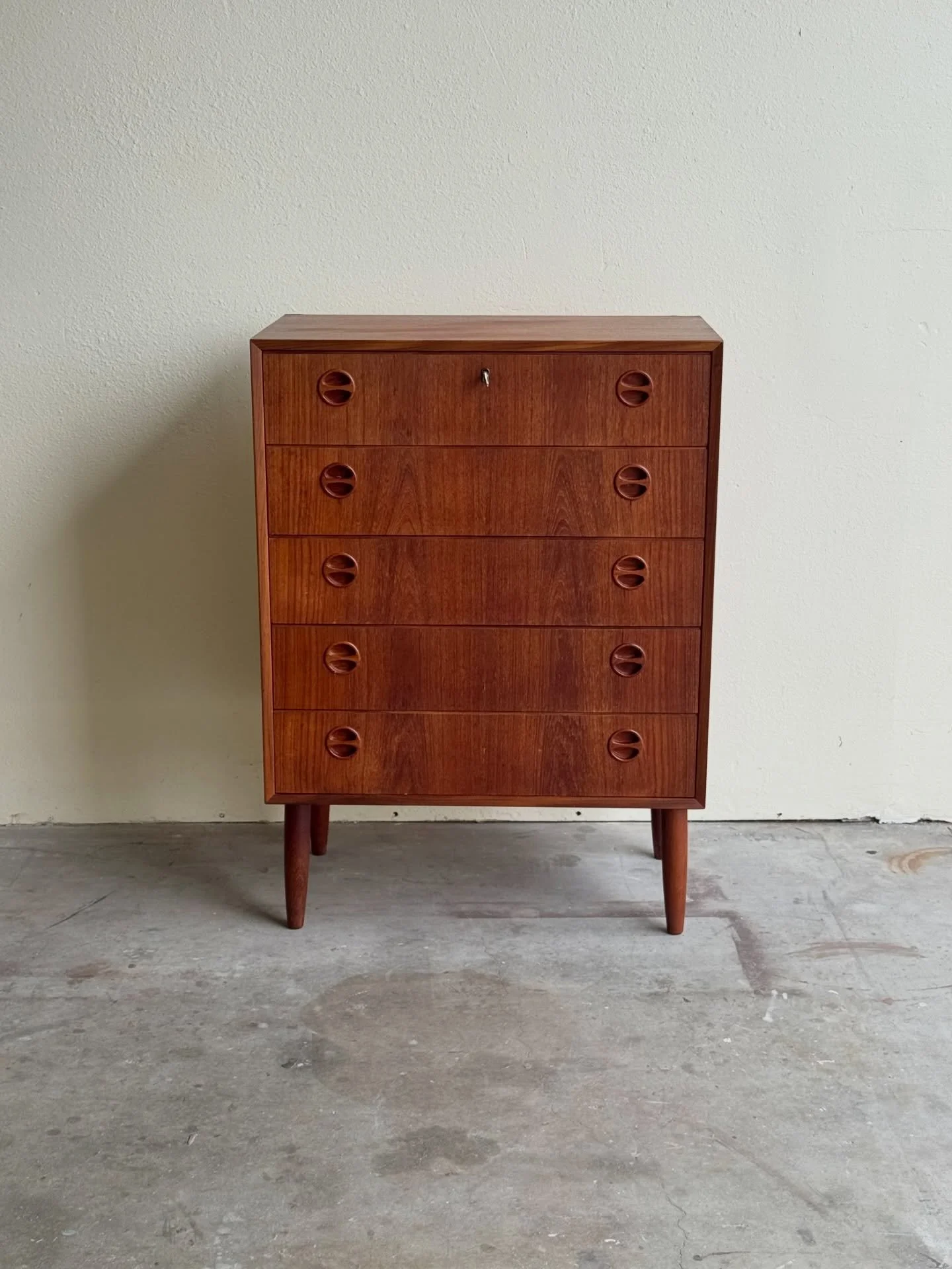 Original mid-century Danish teak highboy dresser from the 1960s, featuring classic Scandinavian modern design. Five smooth-gliding drawers with sculpted recessed pulls, clean lines, and solid tapered legs. Beautiful warm teak grain throughout.

In gr