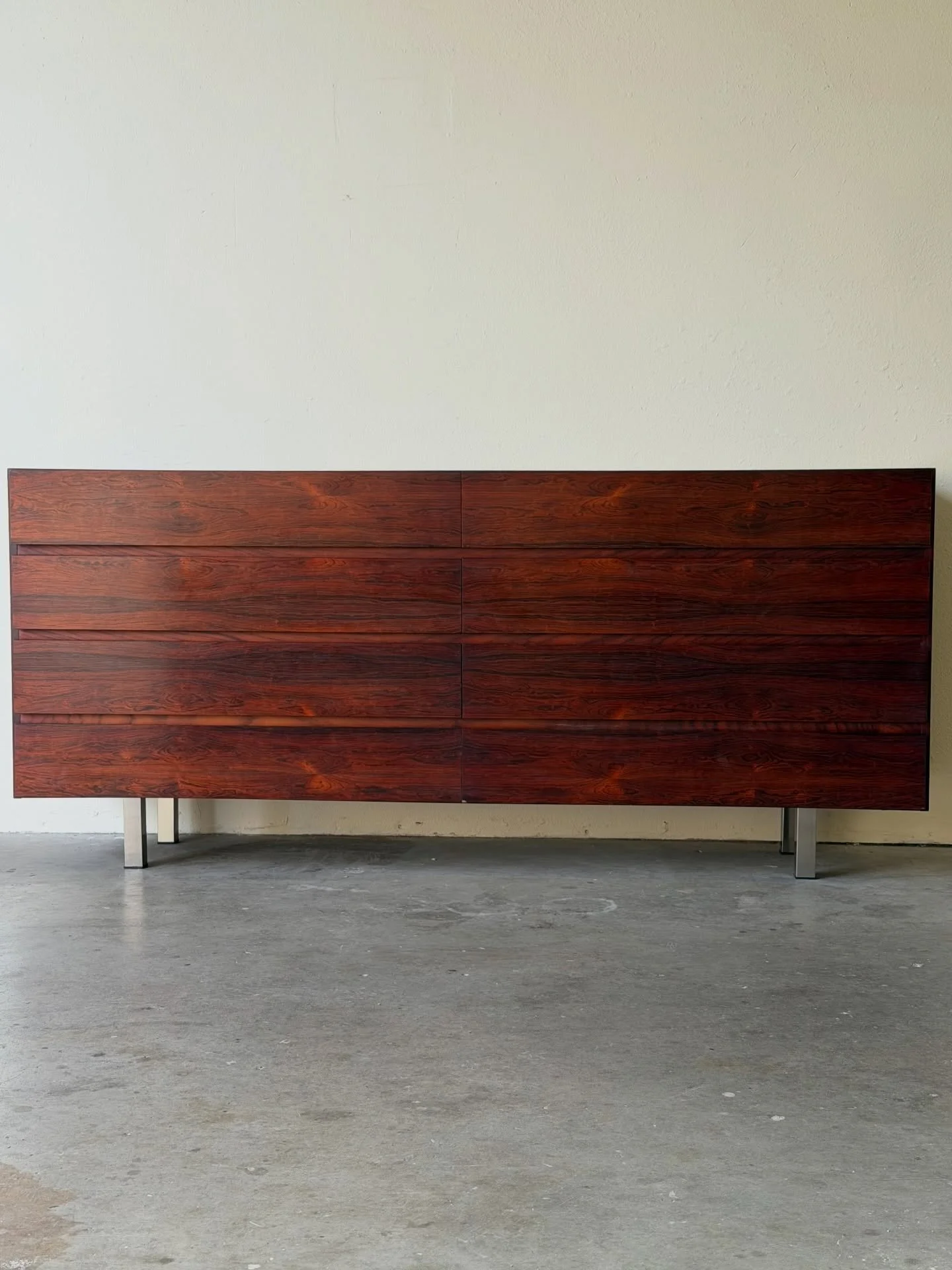 Elegant vintage Danish Mid-Century Modern dresser crafted in richly grained rosewood. This low-profile piece features clean horizontal lines, beautifully matched veneer, and a minimalist silhouette elevated on subtle metal legs, creating a light, arc
