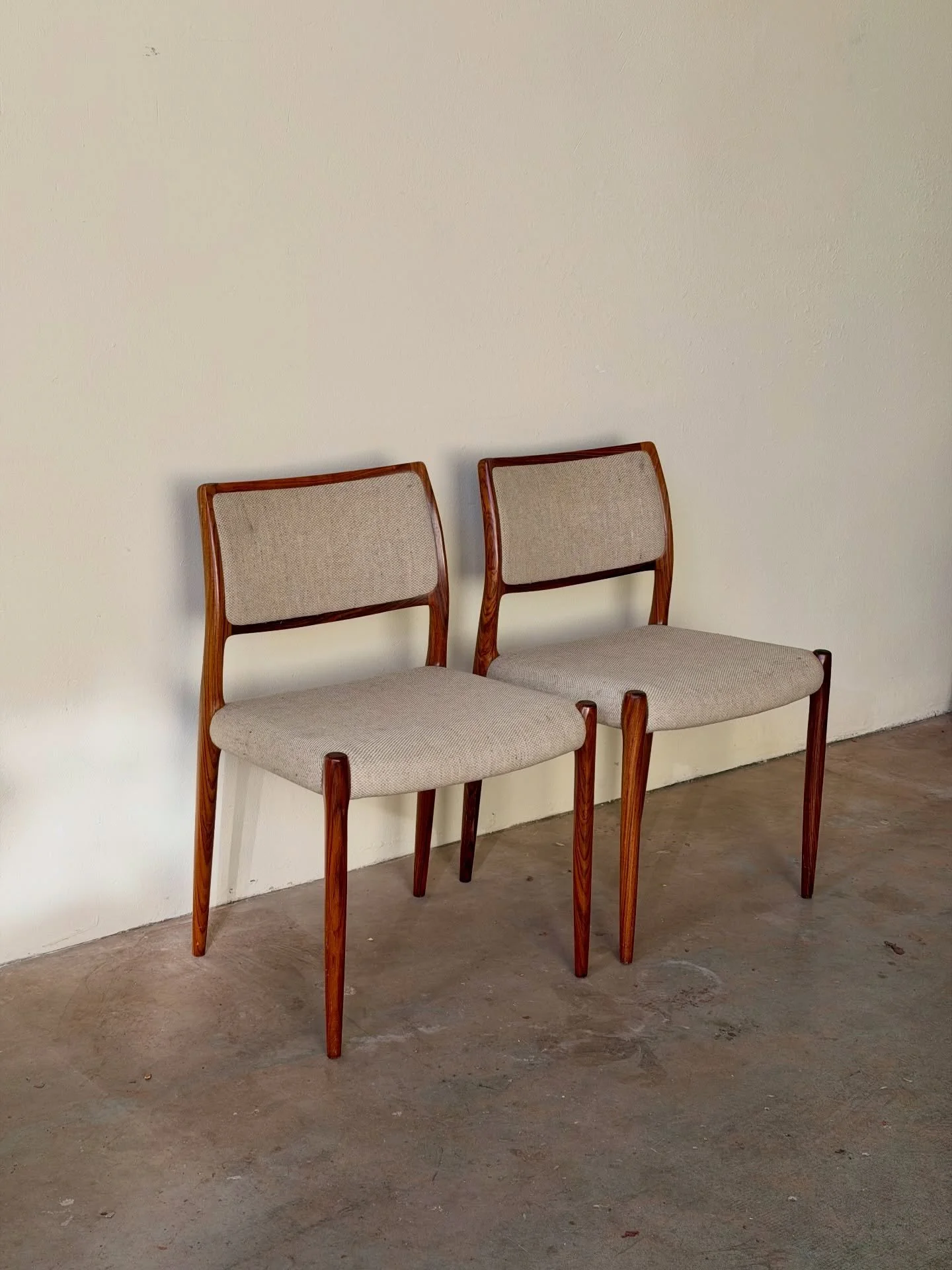 Iconic Danish chairs designed by Niels Otto M&oslash;ller, model No. 80, crafted in solid rosewood. Sculptural frames, curved backrests, and striking grain make them beautiful from every angle.

Upholstered in a soft neutral fabric that complements t