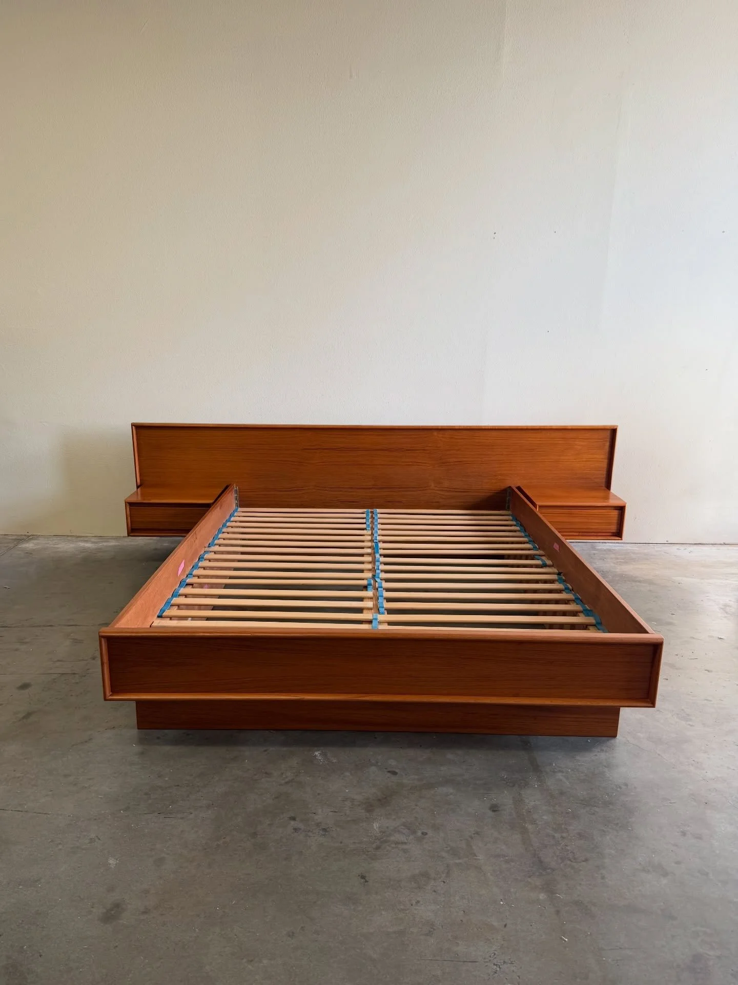 Authentic Mid-Century Danish teak queen platform bed, circa 1960s, featuring a wide architectural headboard with integrated floating nightstands.

The low-profile platform frame and suspended bedside tables create a sleek floating effect while highli