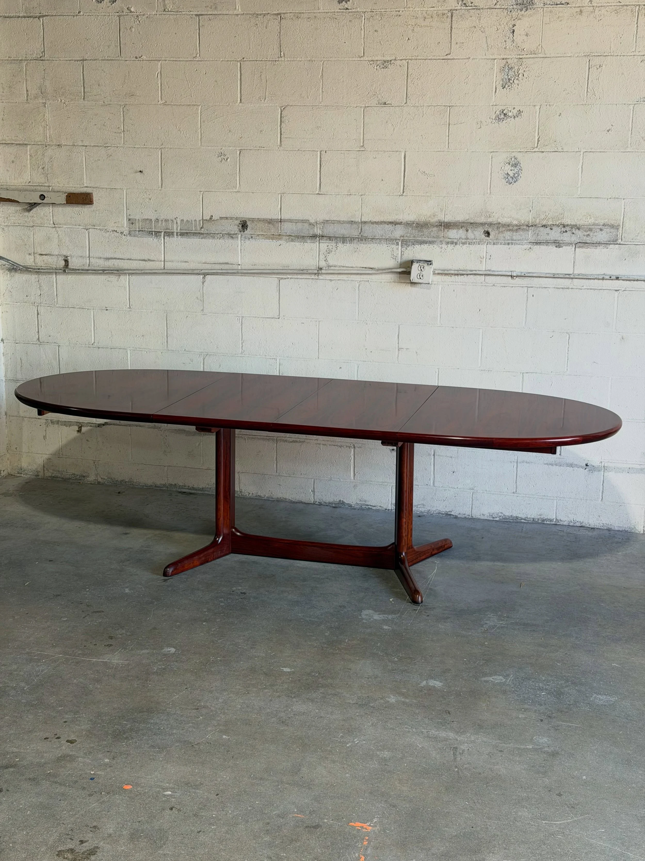 Danish modern extending dining table crafted in richly grained rosewood with a sculptural trestle base and two extension leaves.

The warm rosewood tones and dramatic grain patterns make it stunning even when closed, while the extension system transf