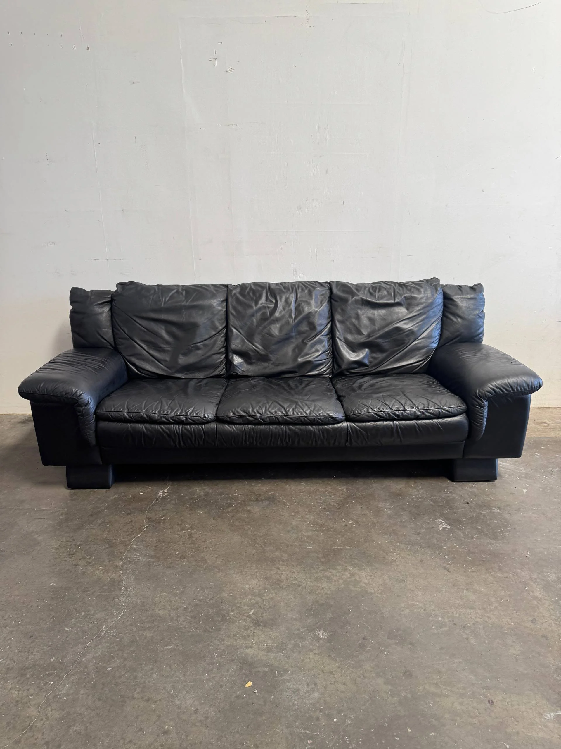 Black leather sofa against a white wall on a concrete floor.