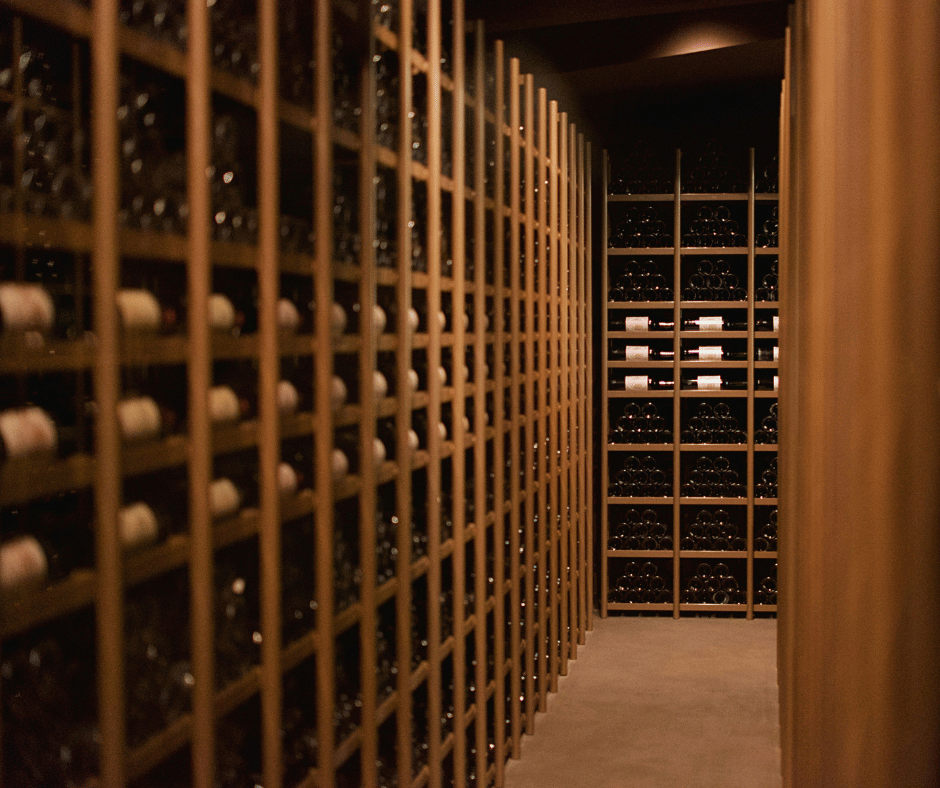 A wine cellar with wooden racks filled with wine bottles, viewed from a corridor.