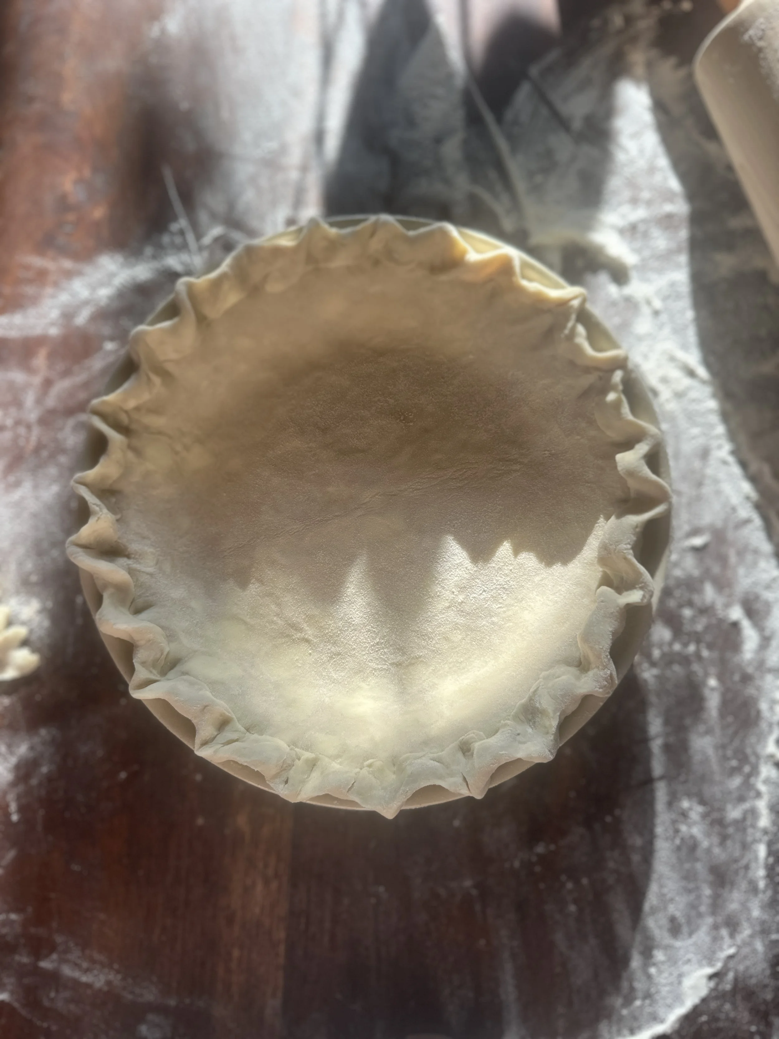 An unbaked pie crust in a ceramic dish on a floured wooden surface.