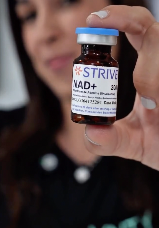 Person holding a small brown vial labeled 'STRIVE NAD+' with a woman in the background.