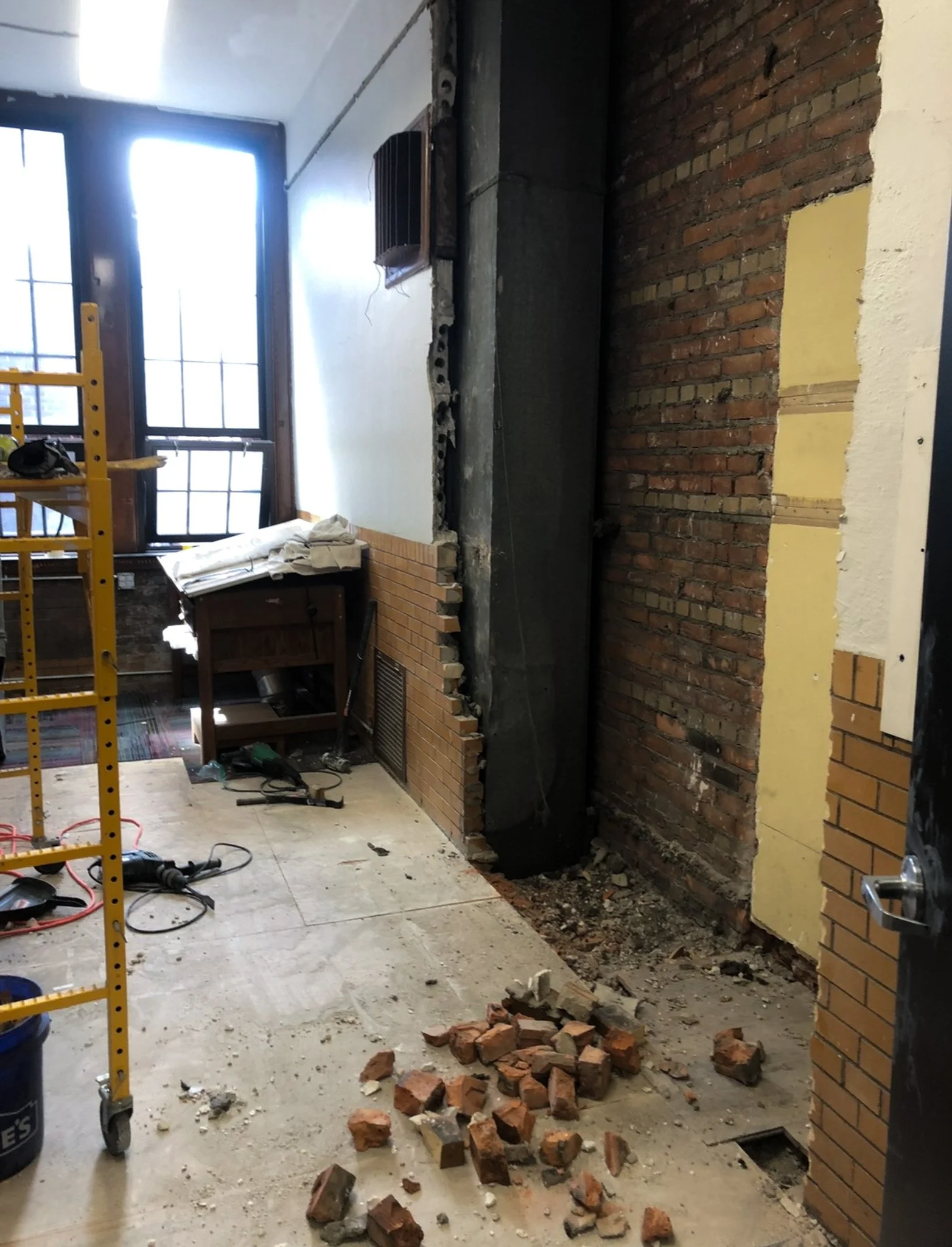 Break room remodel showing exposed brick column and construction debris during demolition