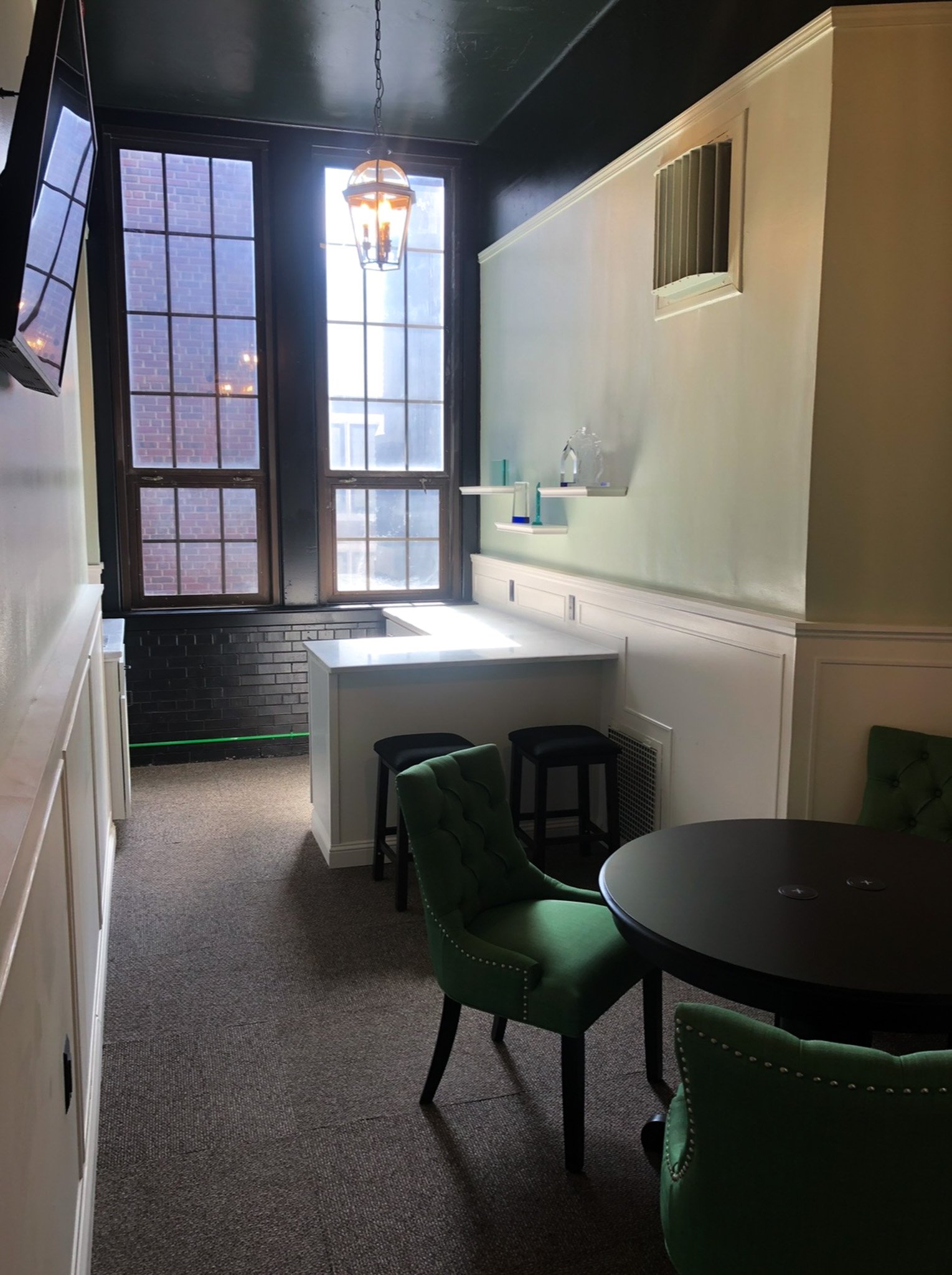 Finished green room with tufted chairs, dark table and built‑in bench under large windows